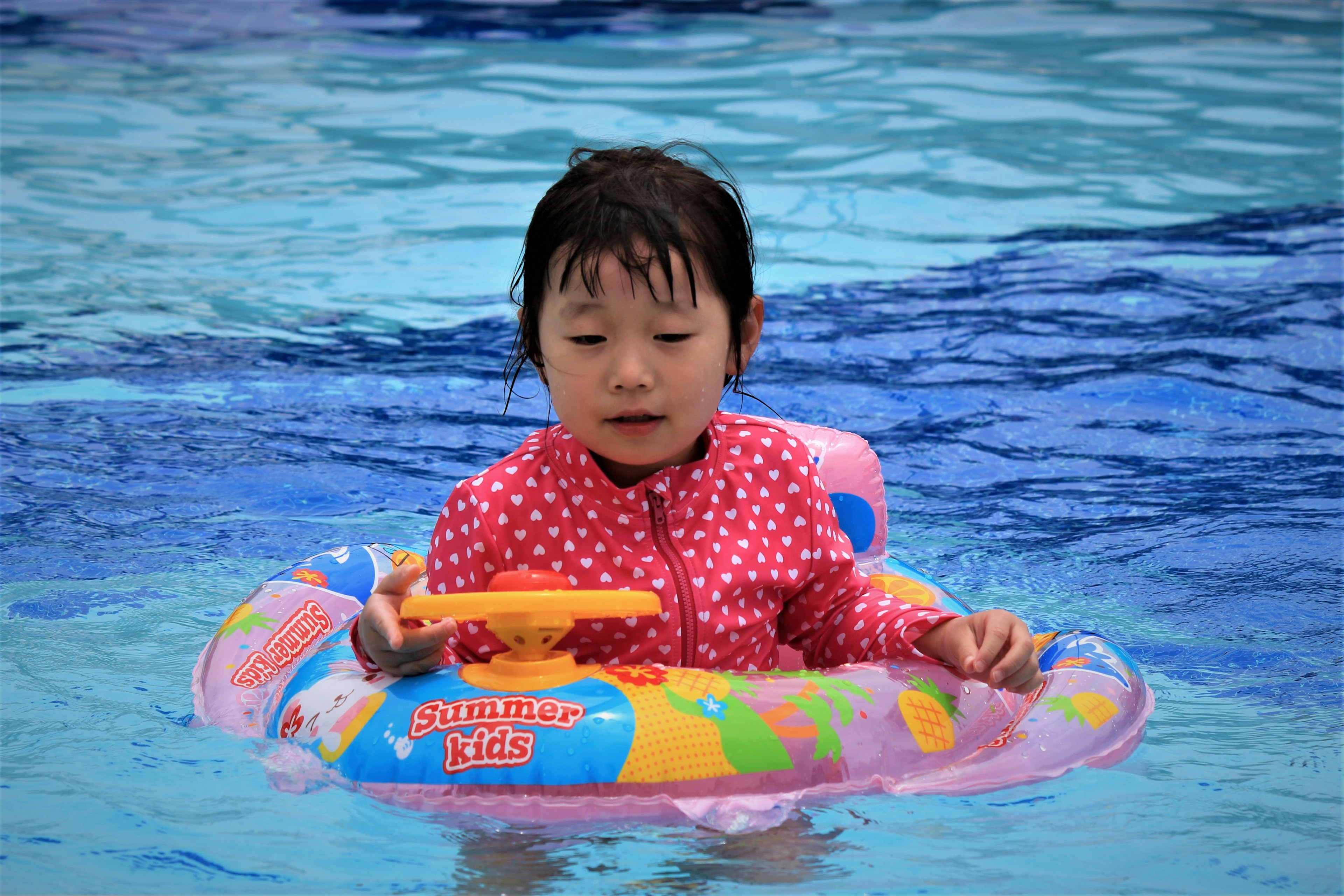 Child playing in water wearing polka dot swimsuit colorful inflatable ring