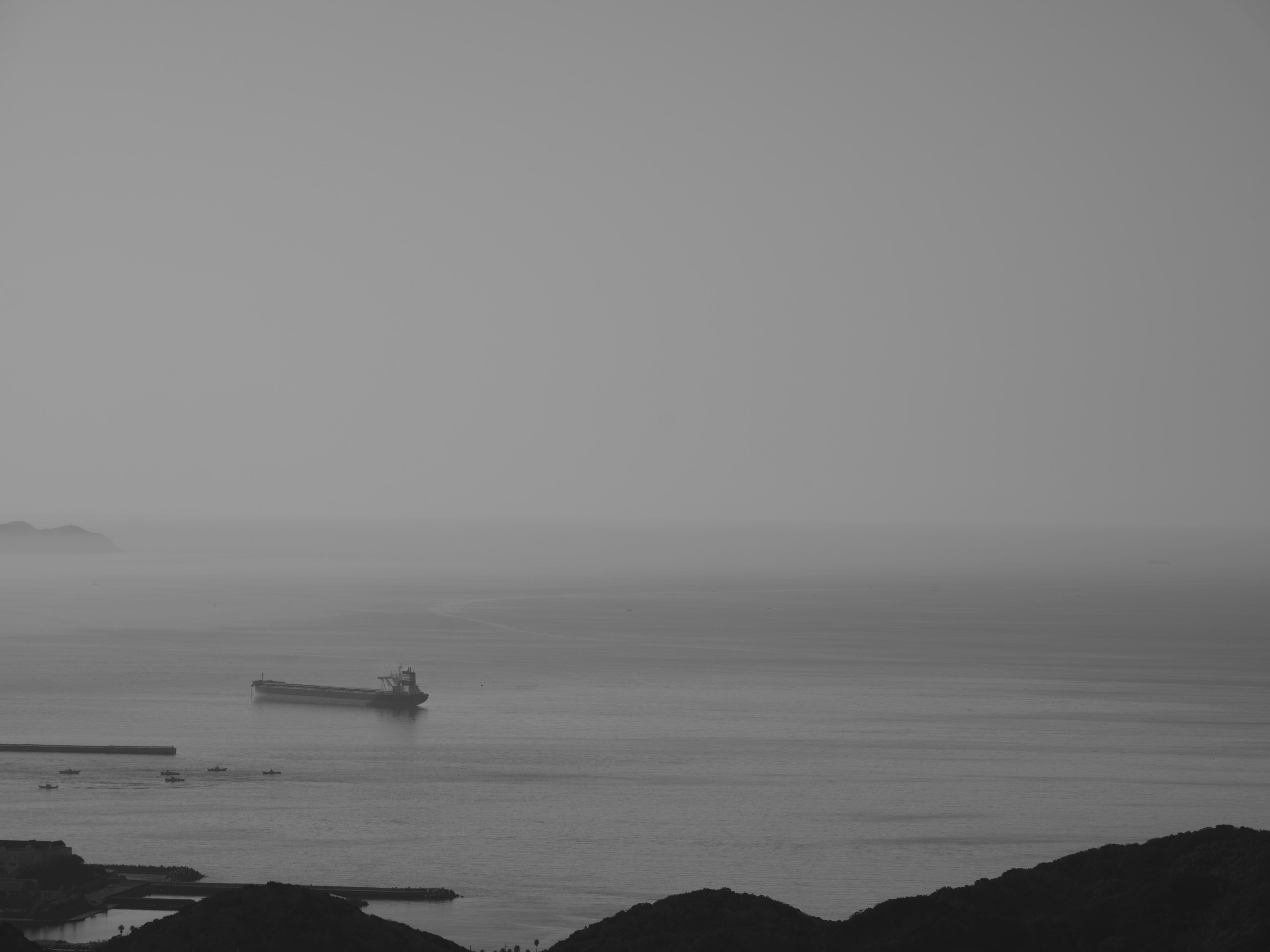 Paisaje marino en blanco y negro con un barco flotando en aguas tranquilas