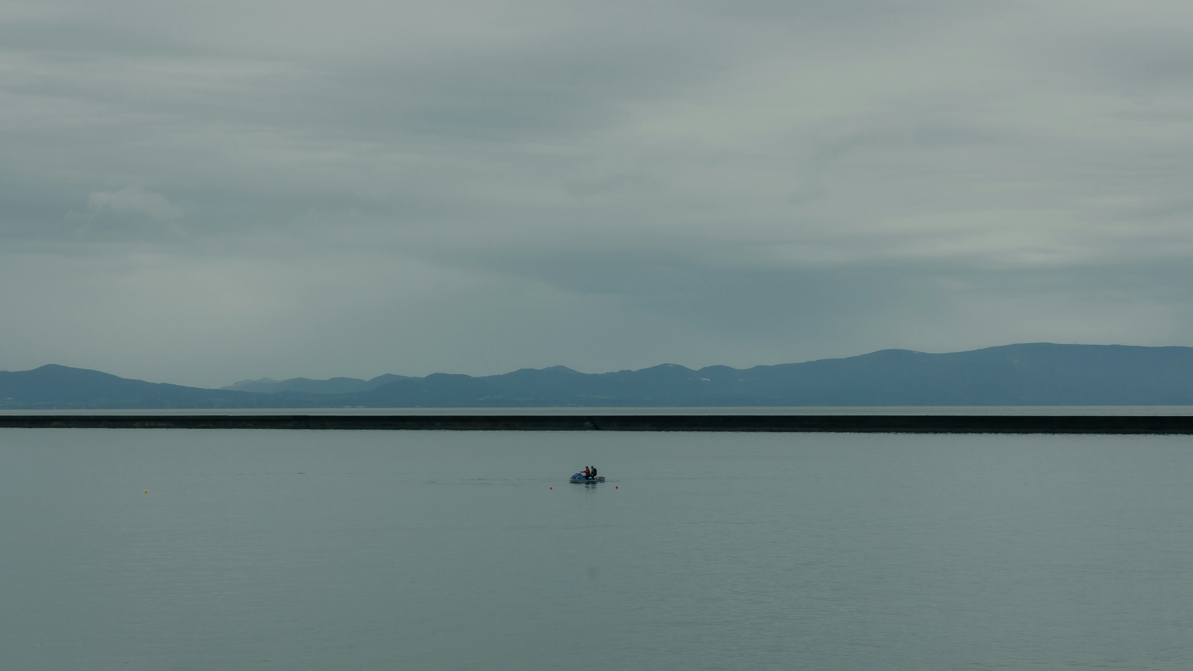 Ein kleines Boot, das auf einem ruhigen See mit entfernten Bergen im Hintergrund schwimmt