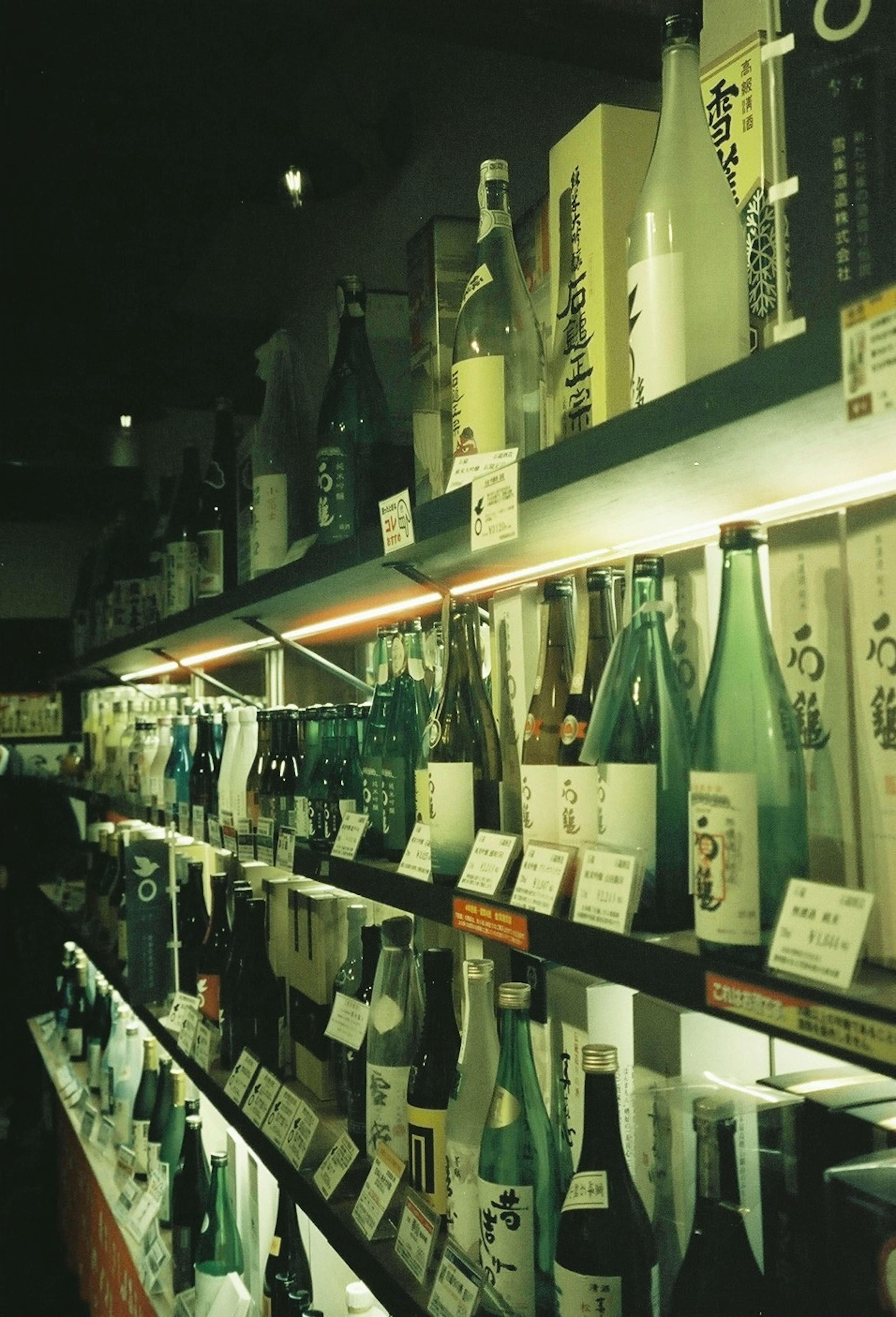 Une vitrine de diverses bouteilles de sake sur des étagères avec un éclairage doux créant une atmosphère chaleureuse