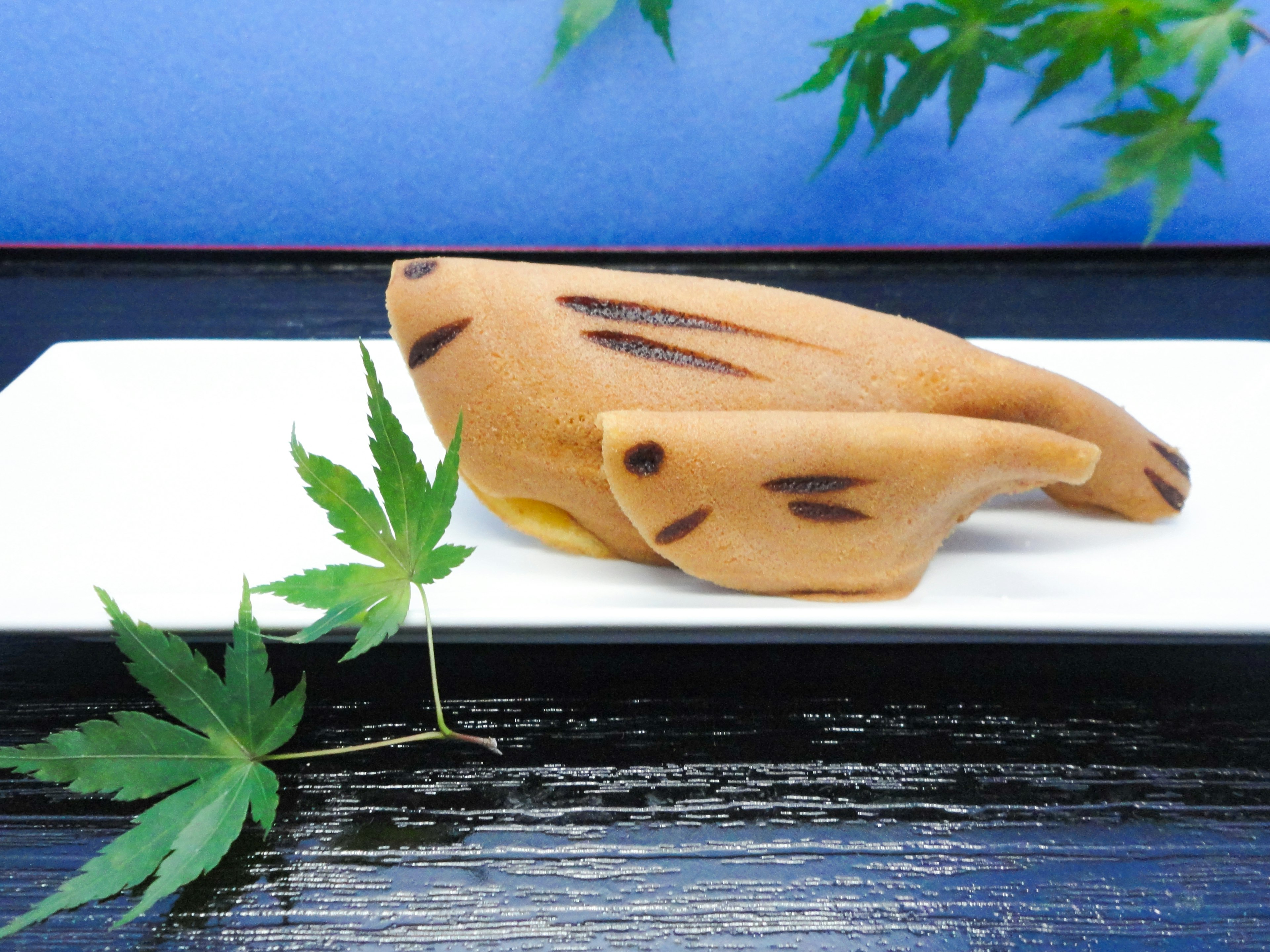 A dessert shaped like a fish on a white plate set against a blue background