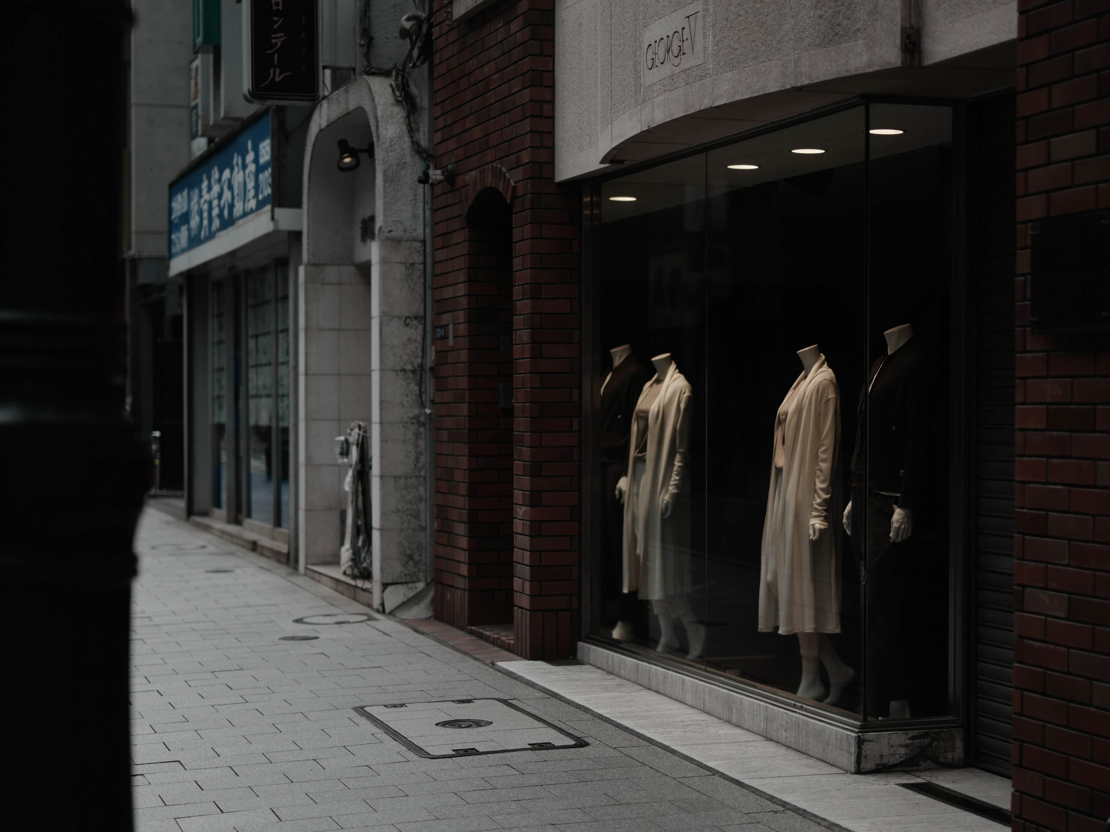 Fashion store window displaying mannequins in coats on a narrow street