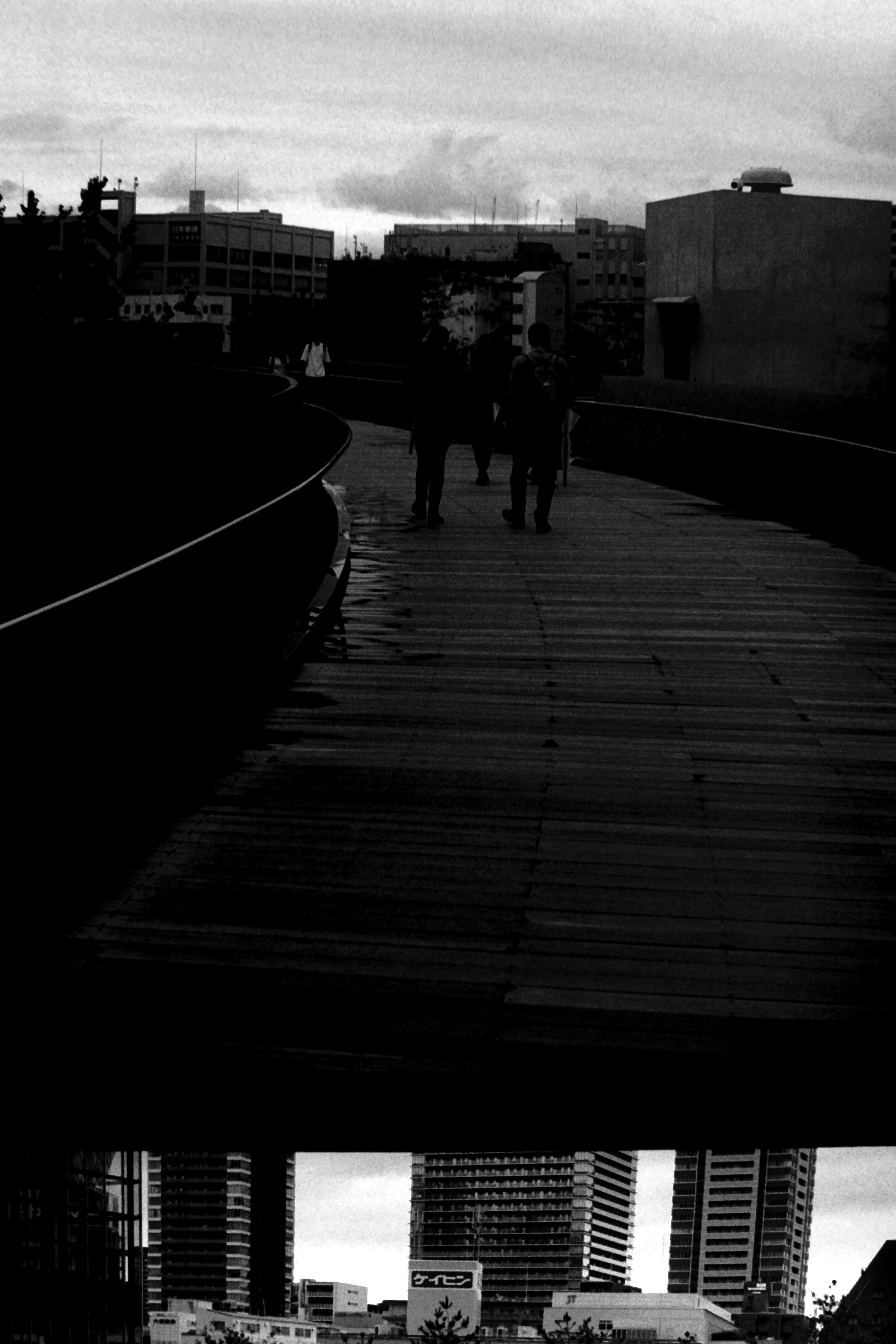 Image de personnes marchant sur un pont en bois noir avec des reflets de la ville en dessous