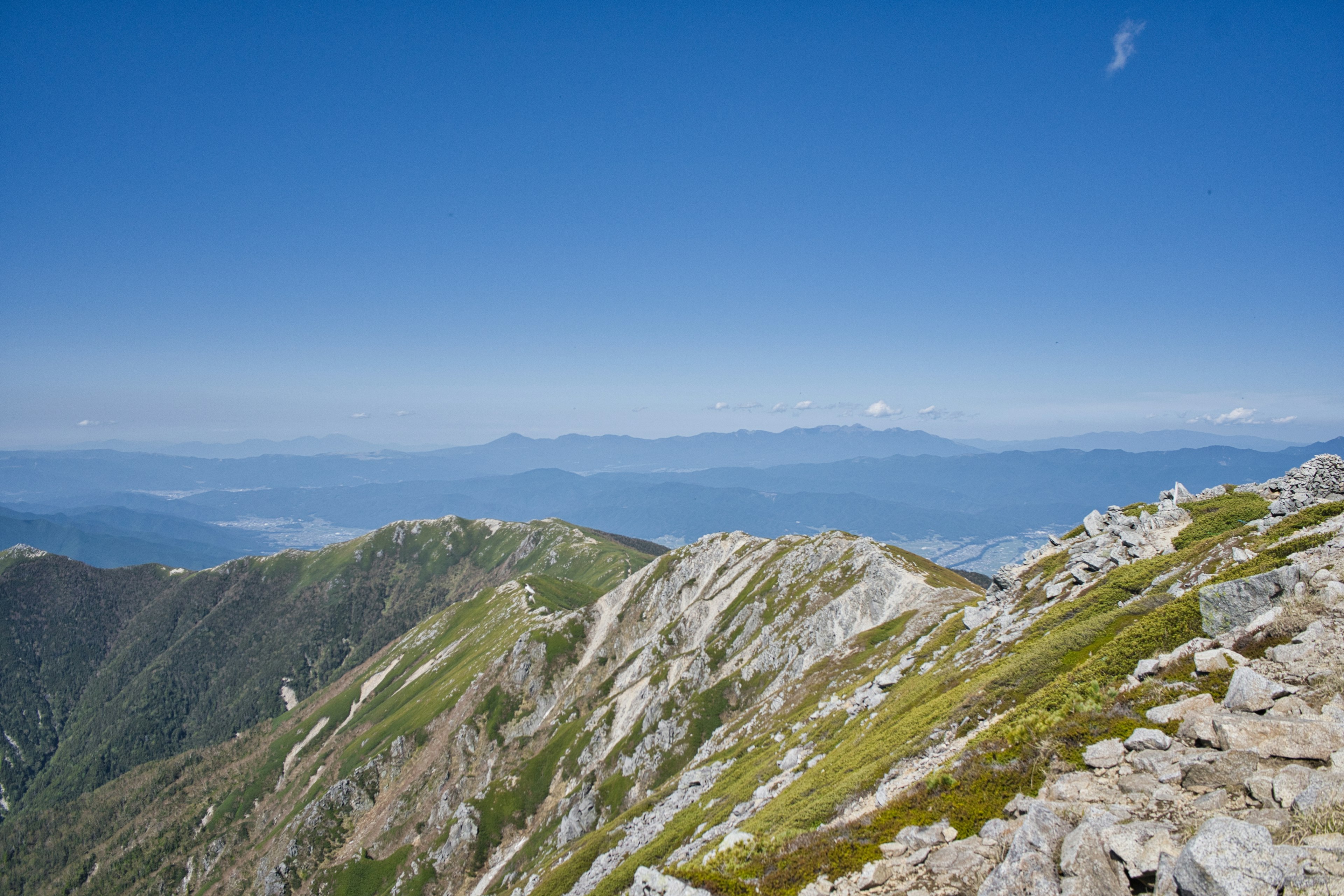 Panoramablick von einem Berggipfel mit blauem Himmel und grünen Hügeln