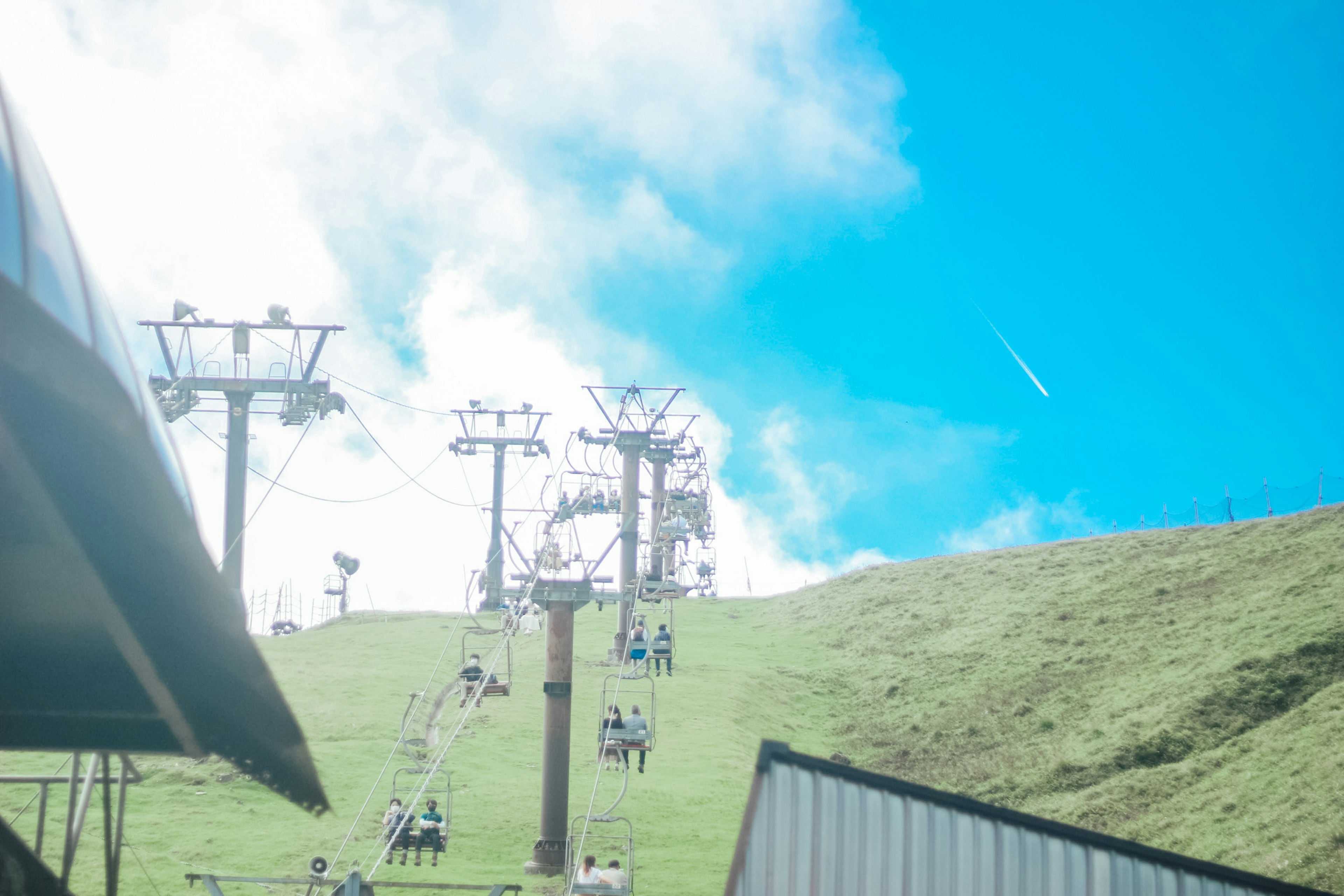 青空の下でリフトに乗る人々と緑の斜面の風景