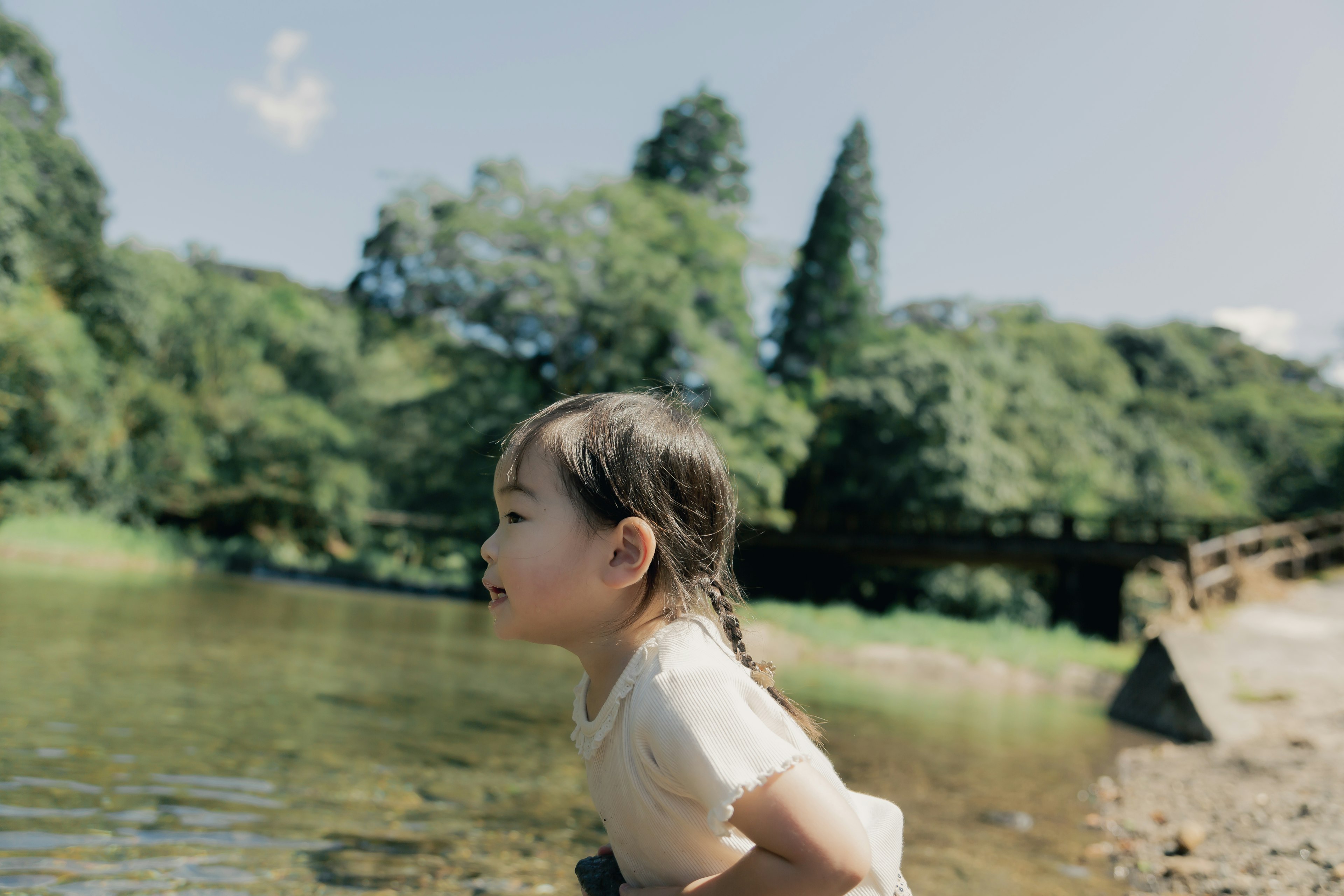 A young girl gazing at the water near a river in a lush green setting