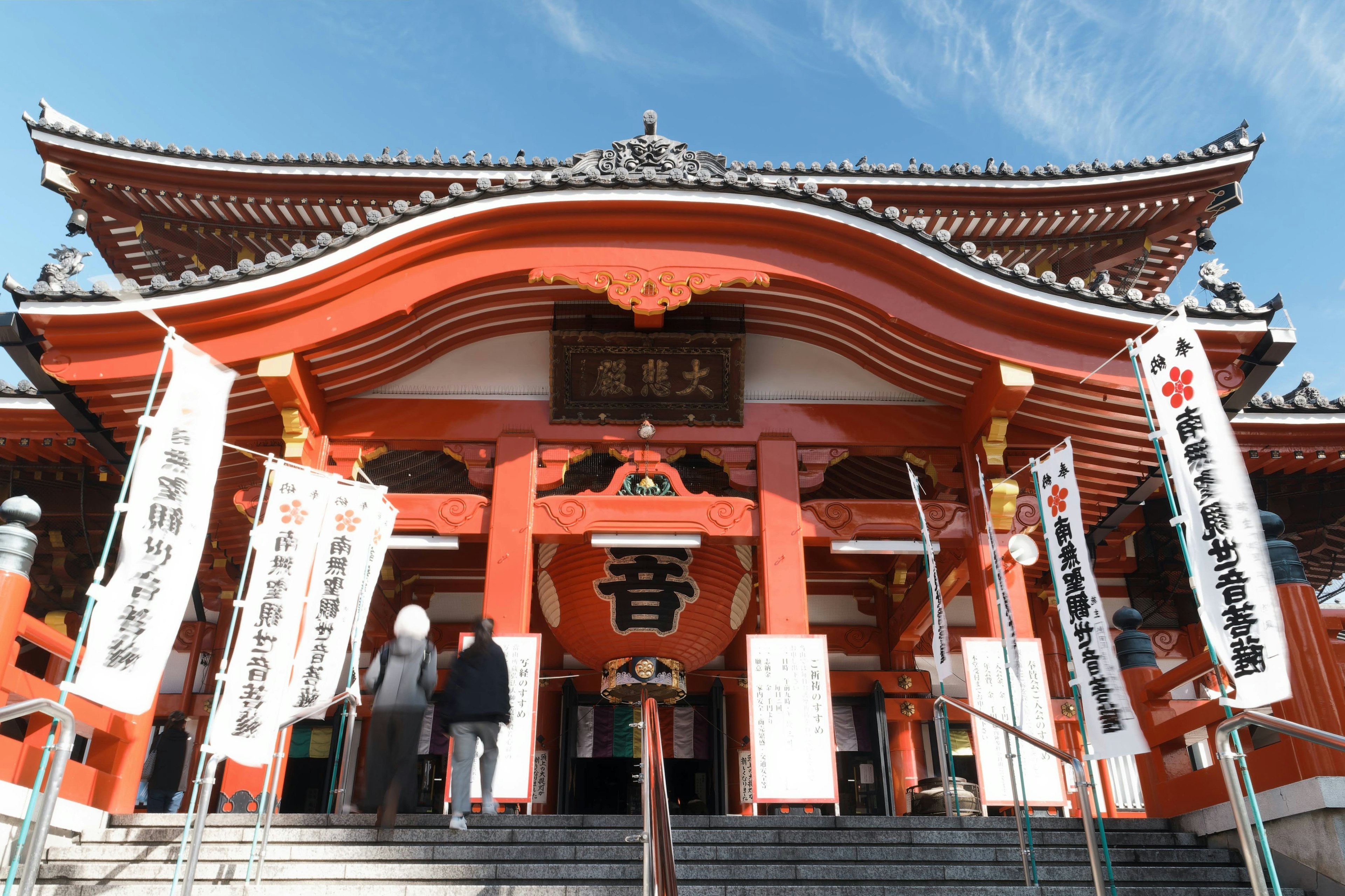 Entrance of a shrine with red roof and people standing by white banners