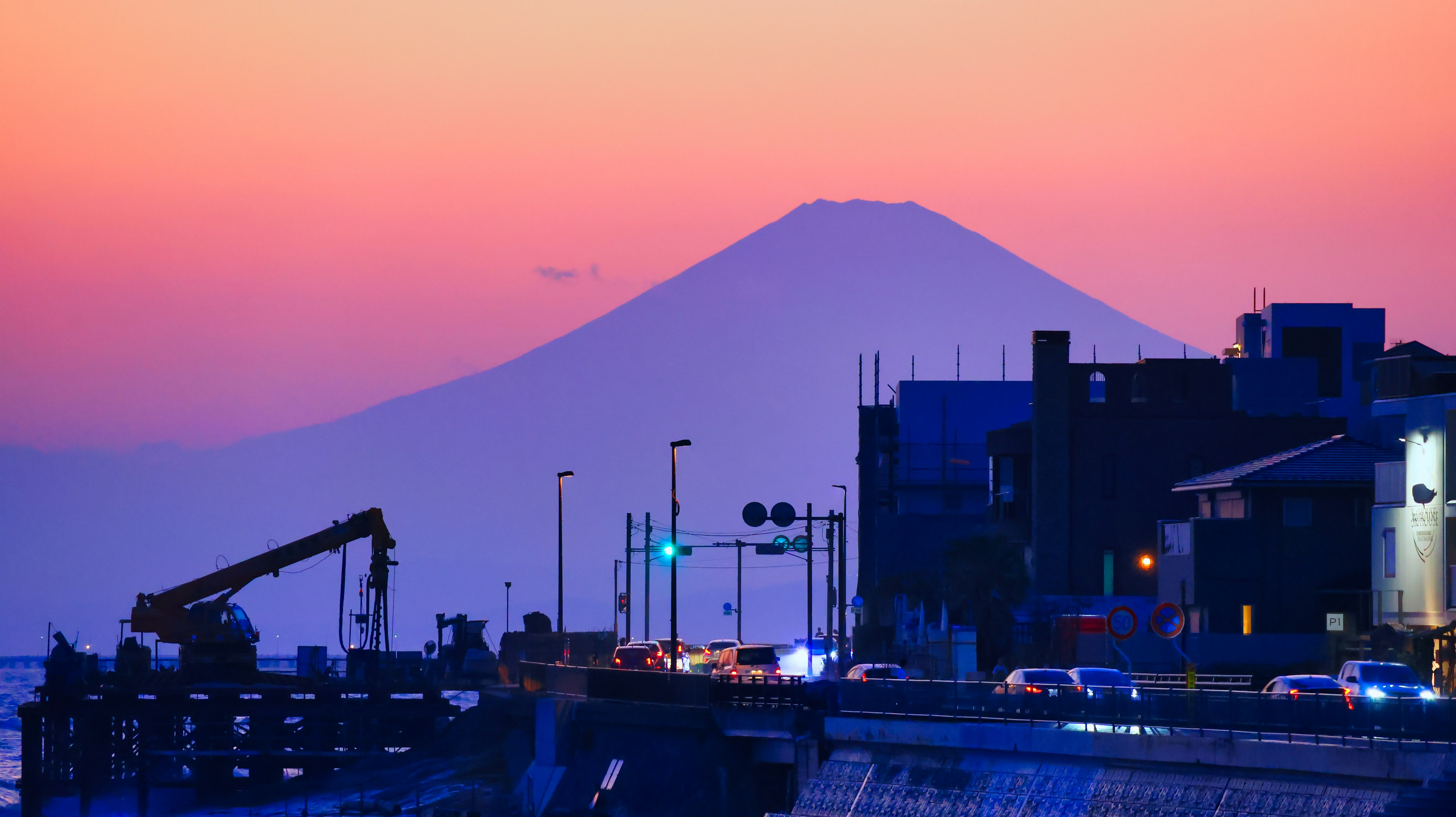 Mount Fuji silhouetted against a colorful sunset with a coastal view