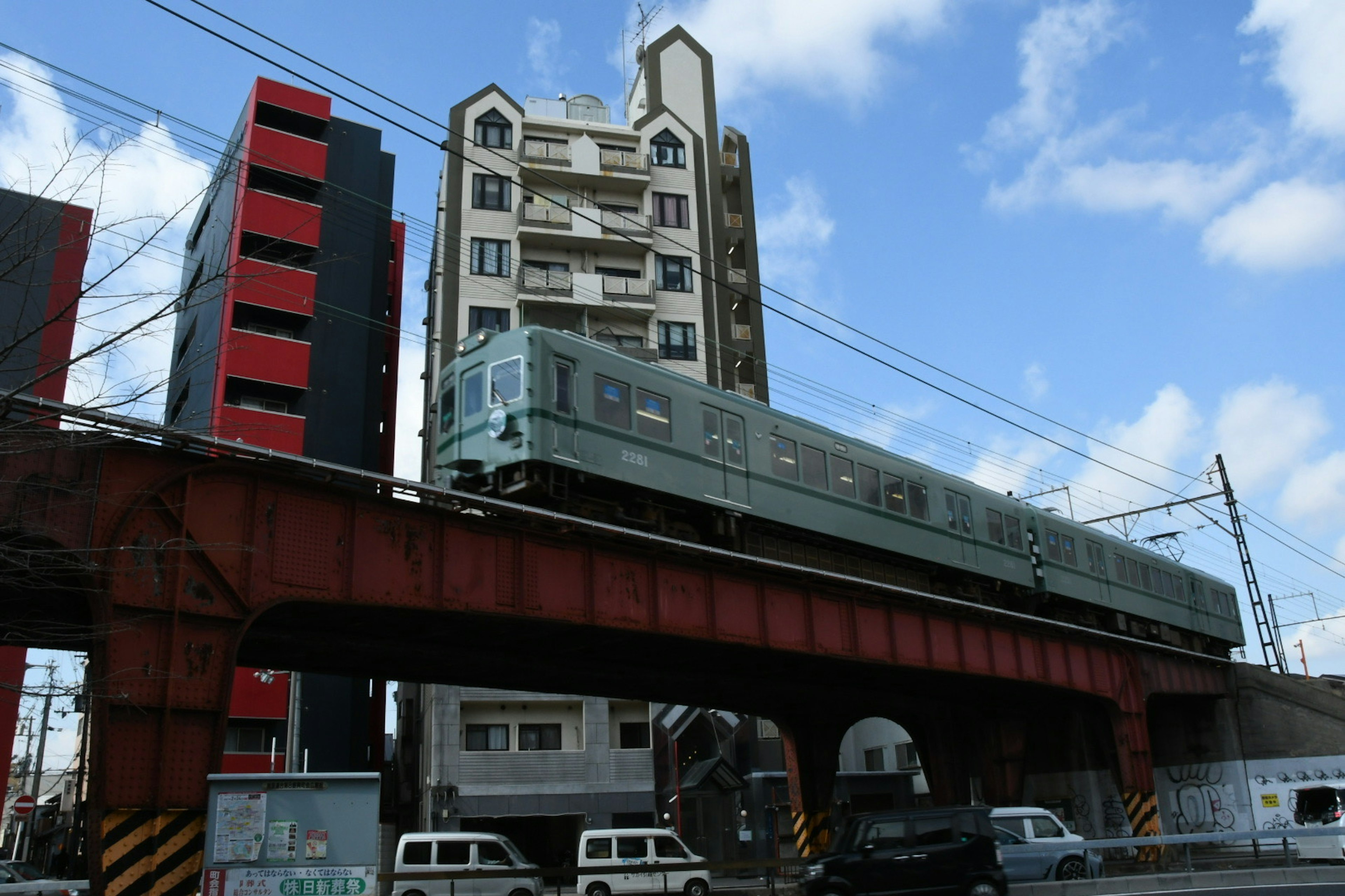 A green train running over a red bridge in an urban landscape