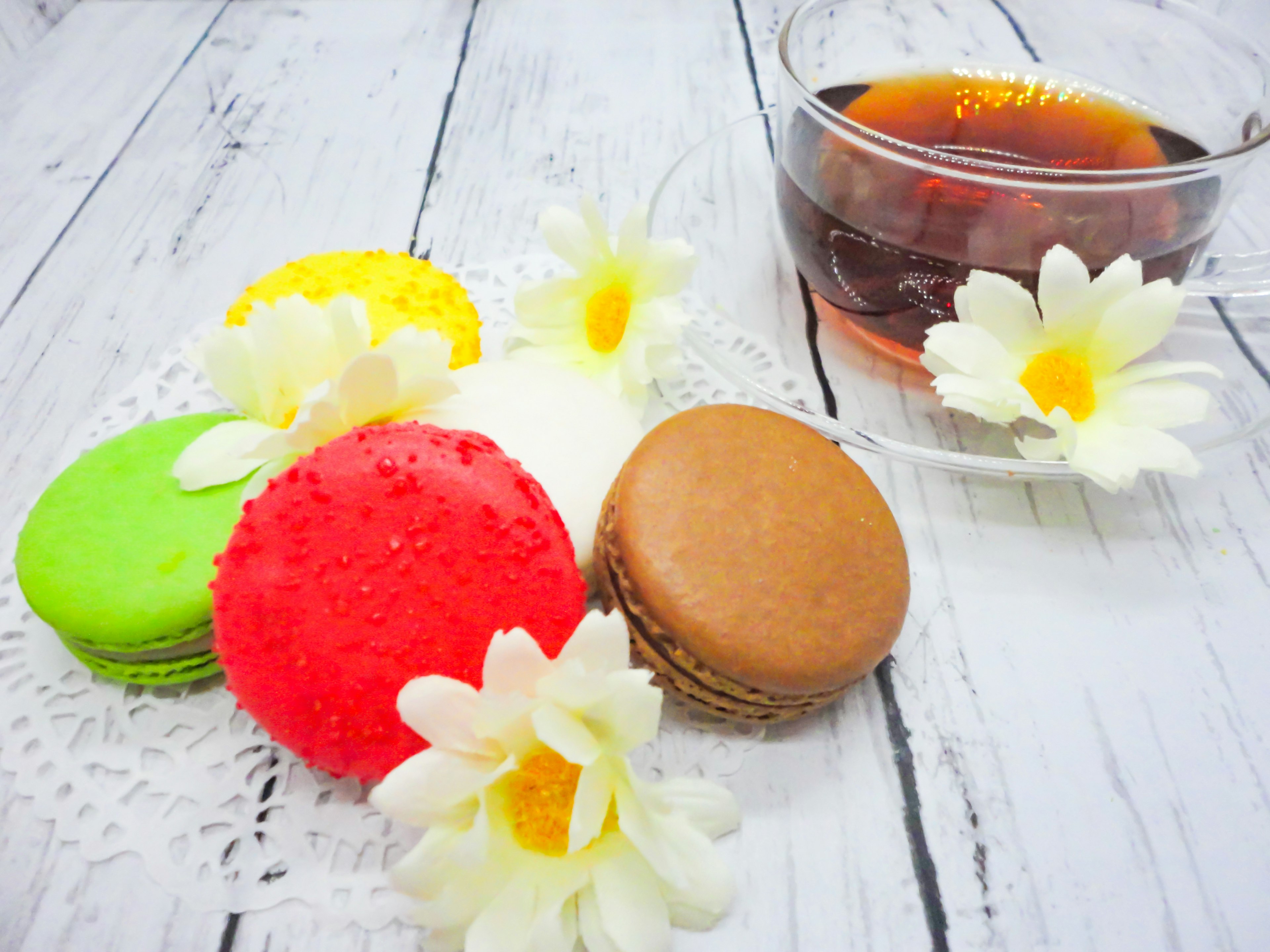 Bunte Macarons und Tee auf einem Holztisch mit weißen Blumen