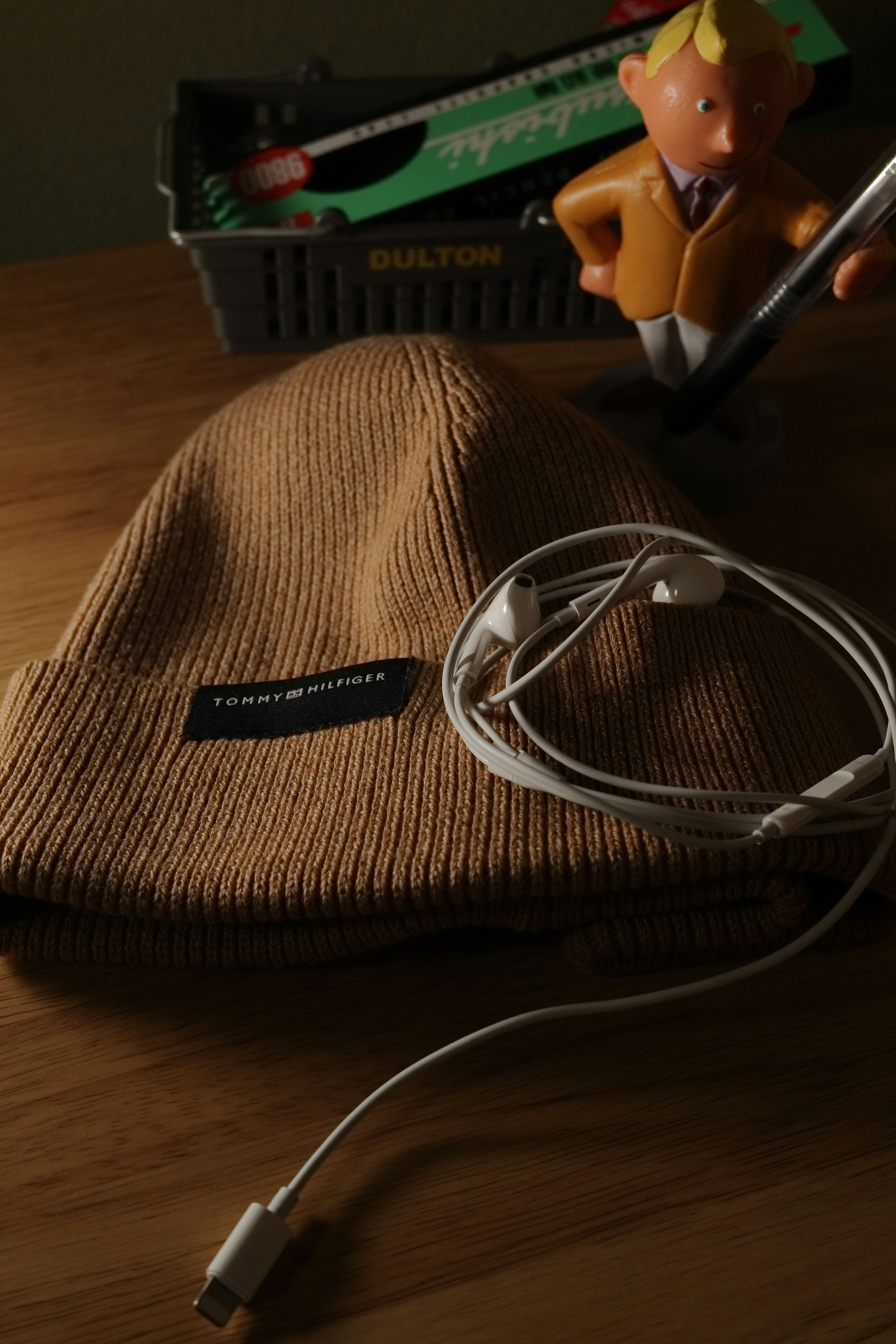 Beige beanie, white earphones, and a yellow character figurine on a table