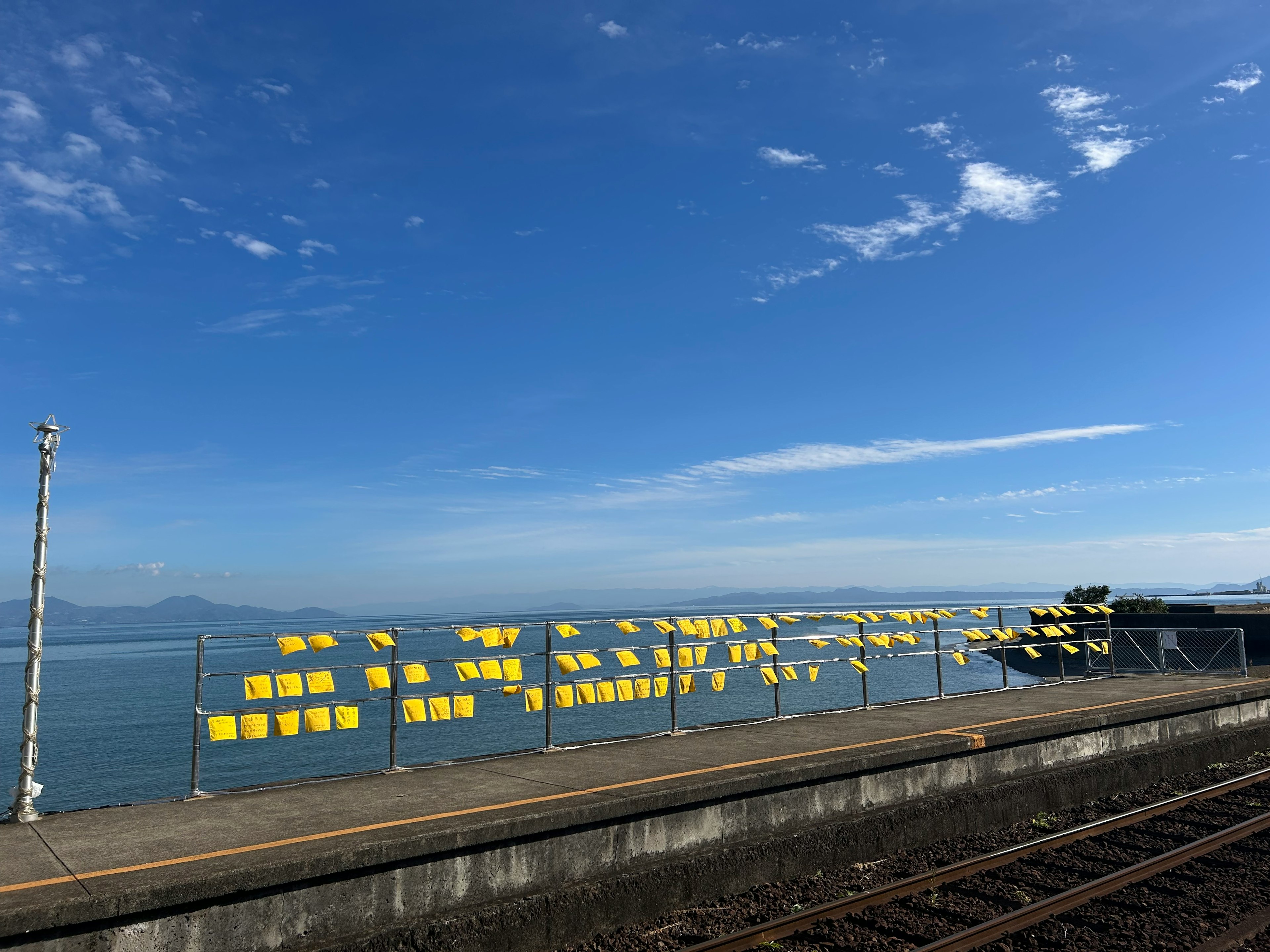 Pemandangan indah langit biru dan lautan dengan kain kuning yang menggantung di sepanjang pagar