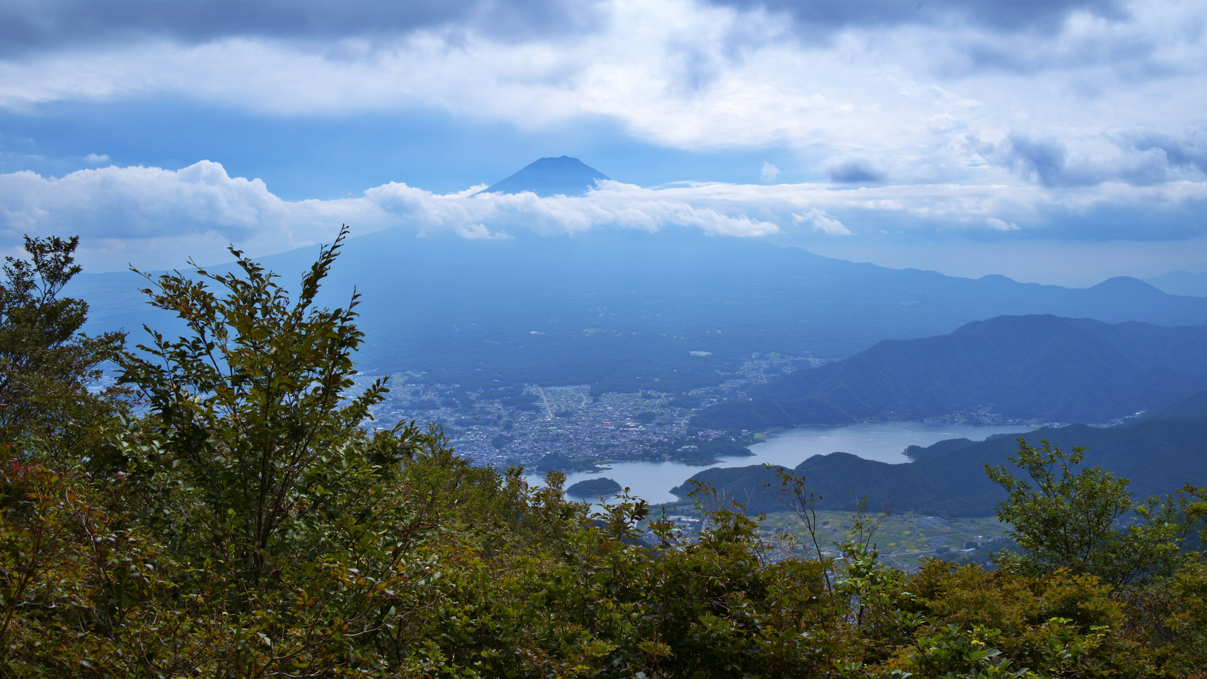 Vista panoramica delle montagne circondate da un cielo blu e nuvole con il Monte Fuji sullo sfondo