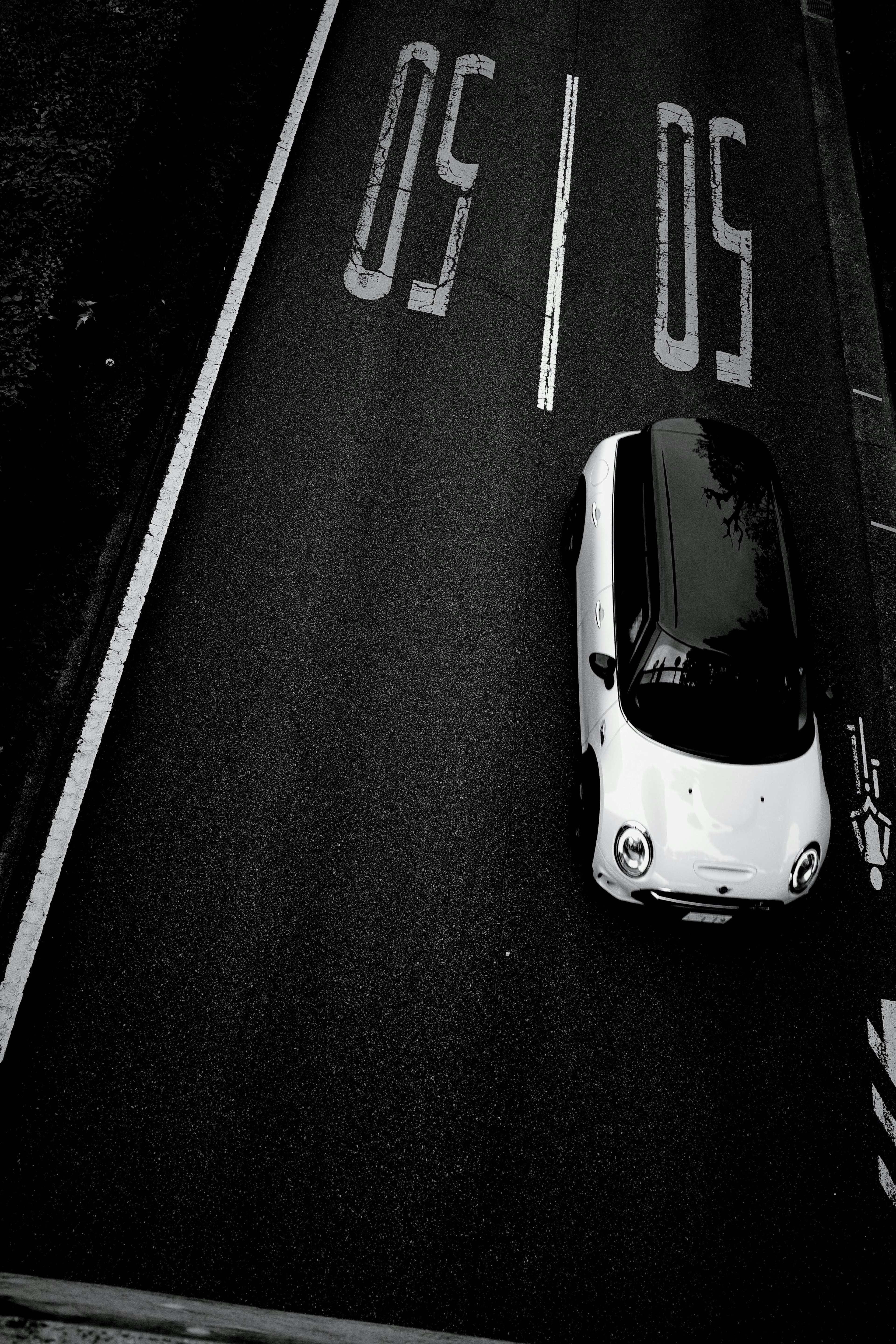 Una piccola auto bianca e nera che guida vicino a un segnale di limite di velocità di 50 km sulla strada