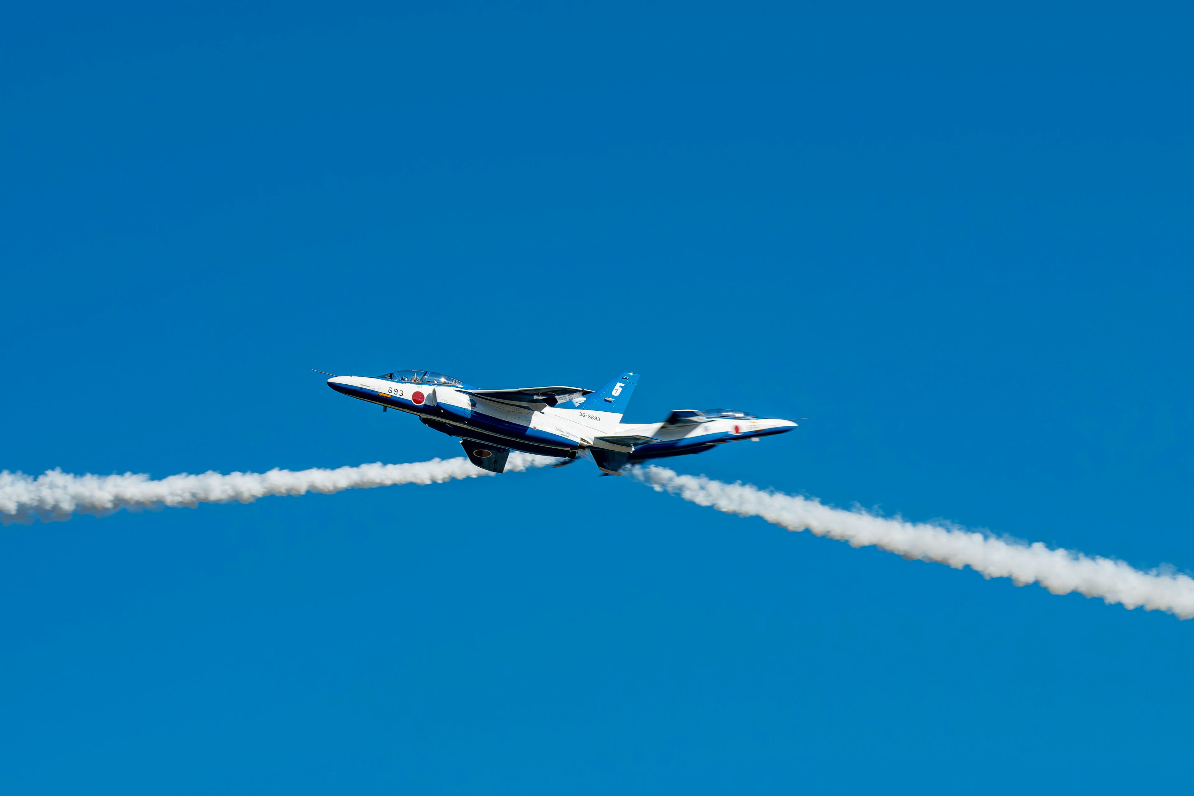 Flugzeug fliegt vor blauem Himmel und hinterlässt weiße Kondensstreifen