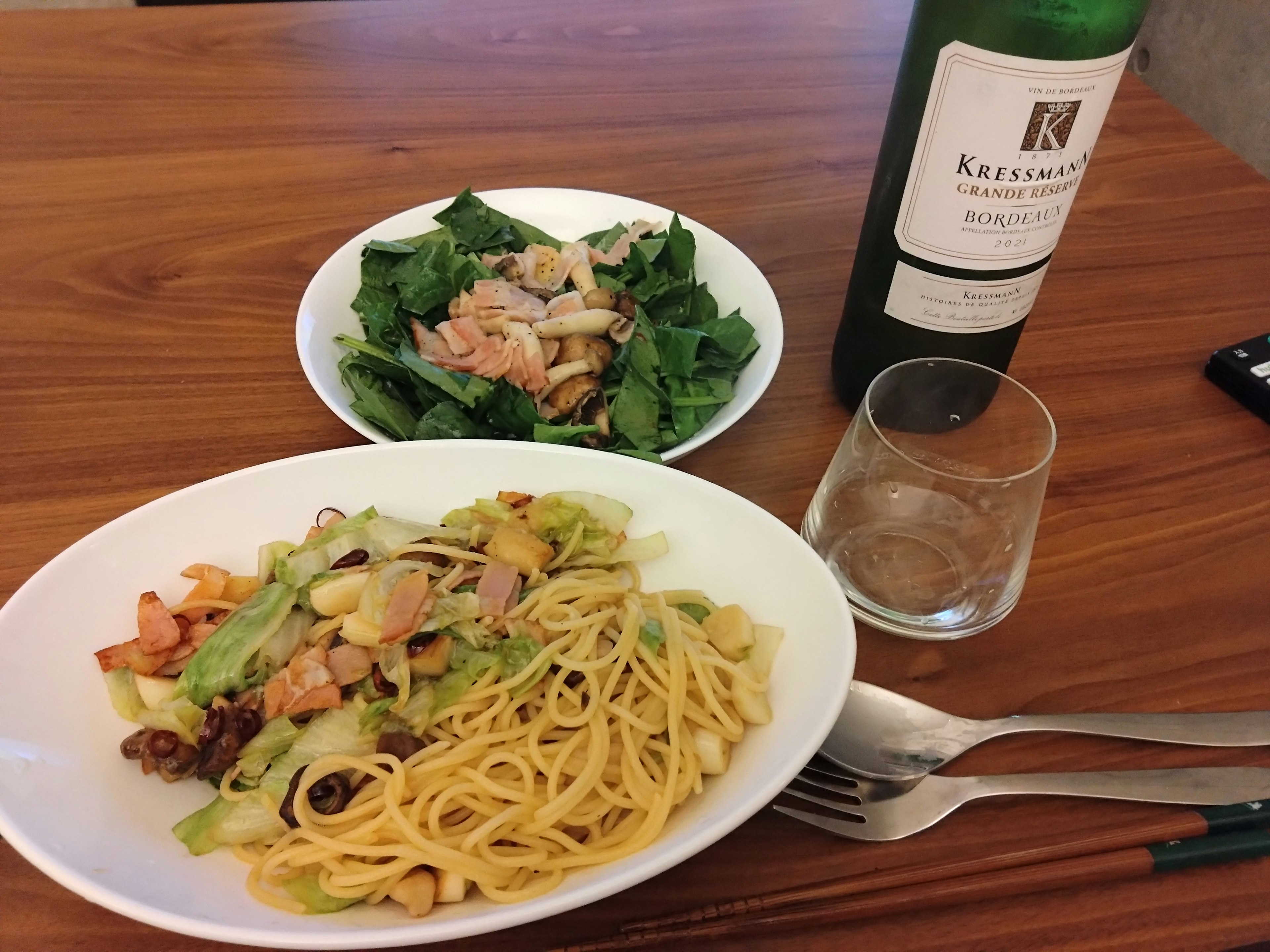 Plato de pasta con verduras y una ensalada junto a una botella de vino sobre una mesa de madera