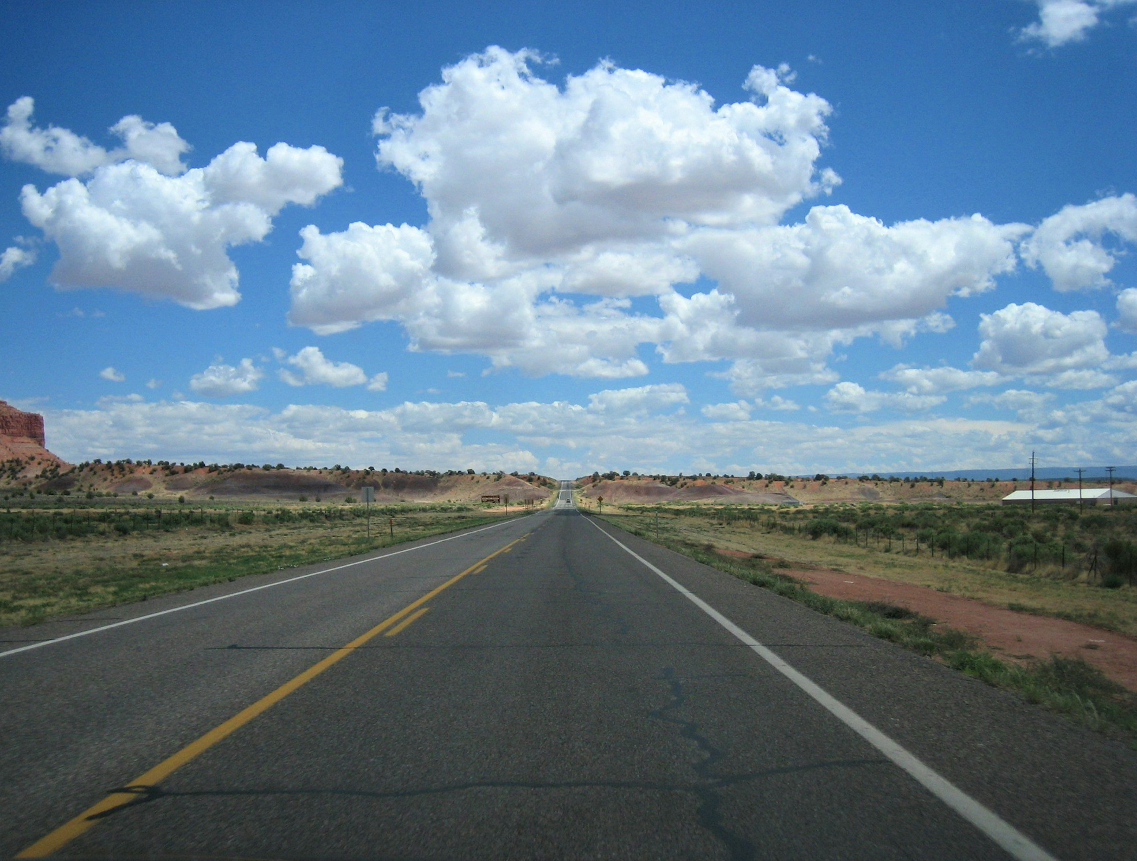 Route droite s'étendant à l'horizon sous un ciel bleu avec des nuages blancs moelleux