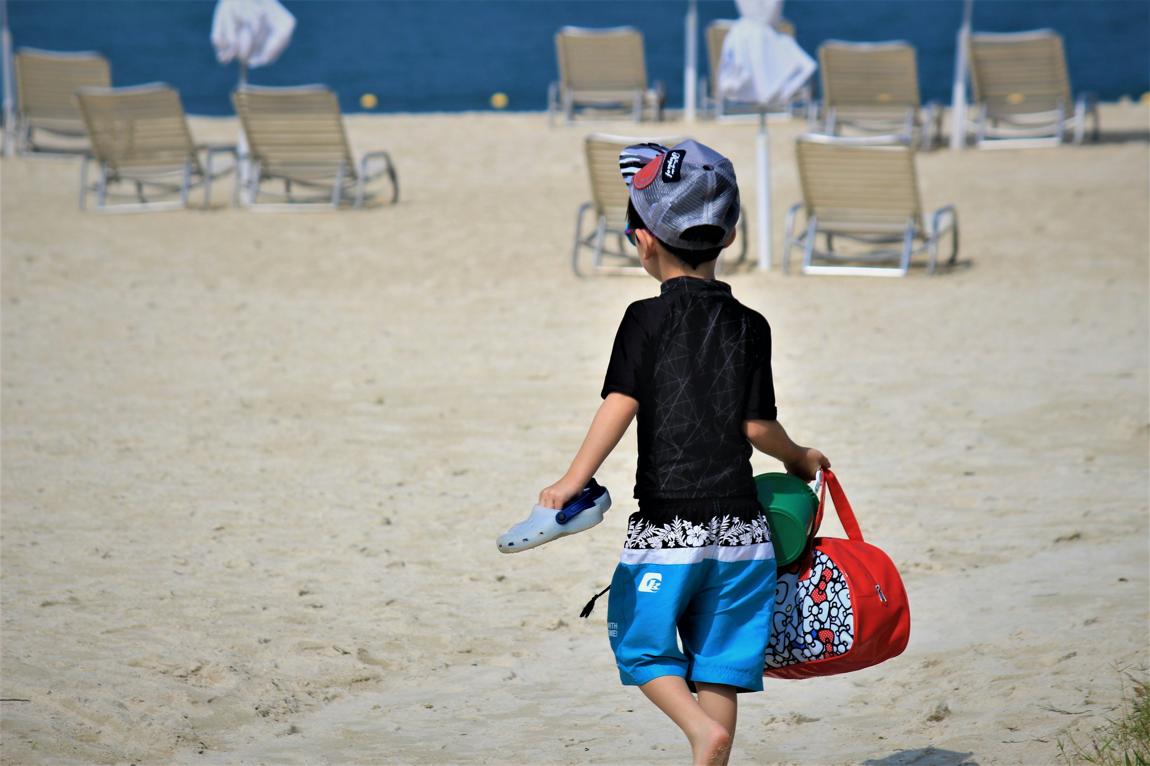 Un bambino che cammina sulla spiaggia con una borsa