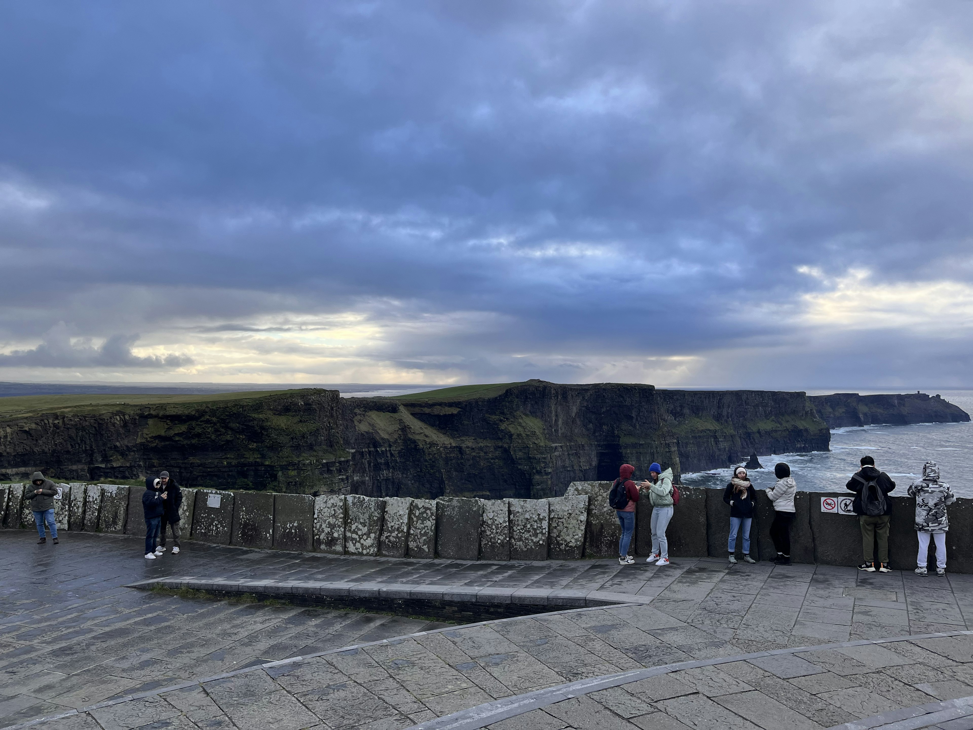 Touristen, die von einem Aussichtspunkt auf Klippen und raues Meer blicken