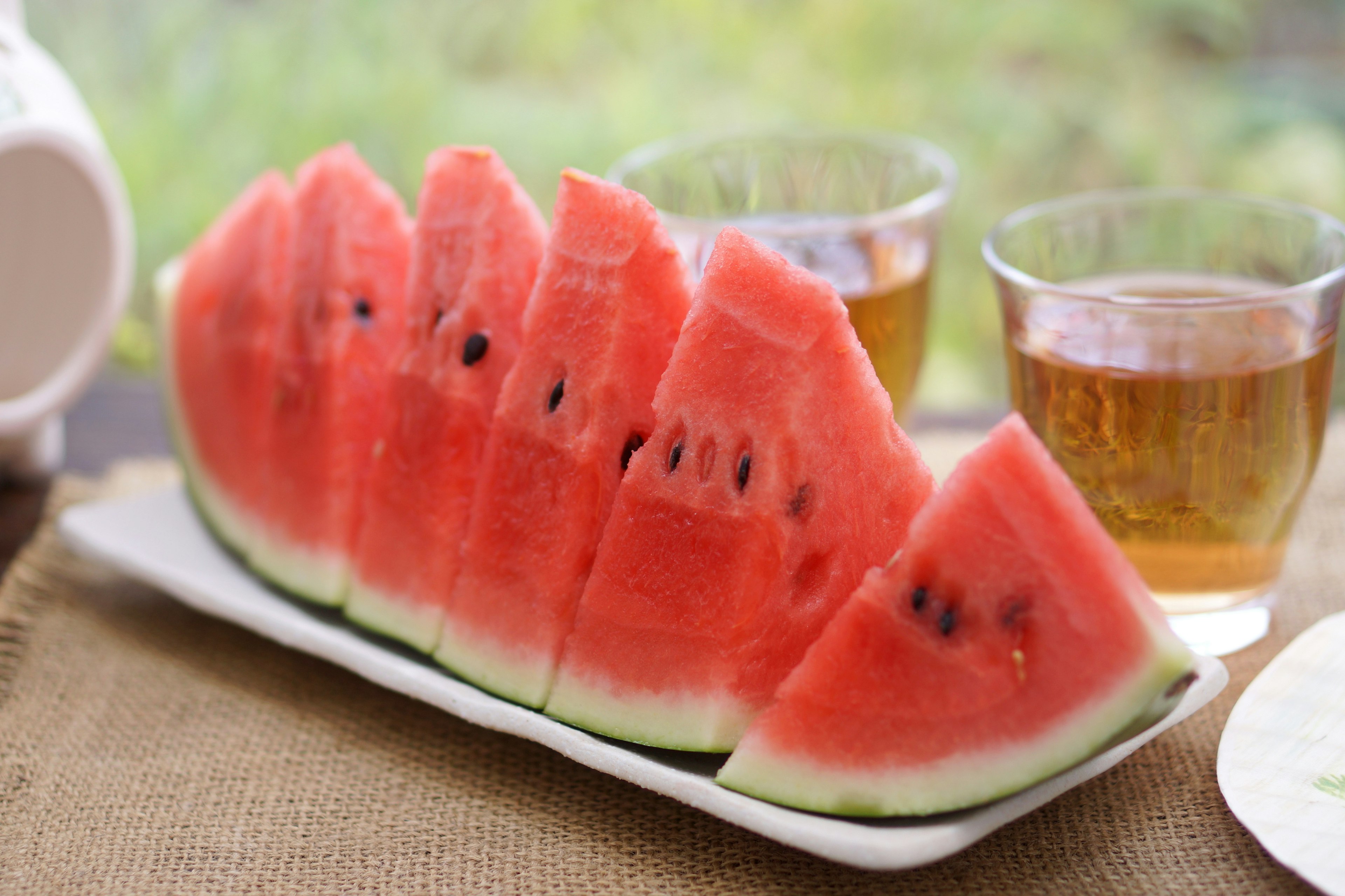 Sliced watermelon on a plate with glasses in the background