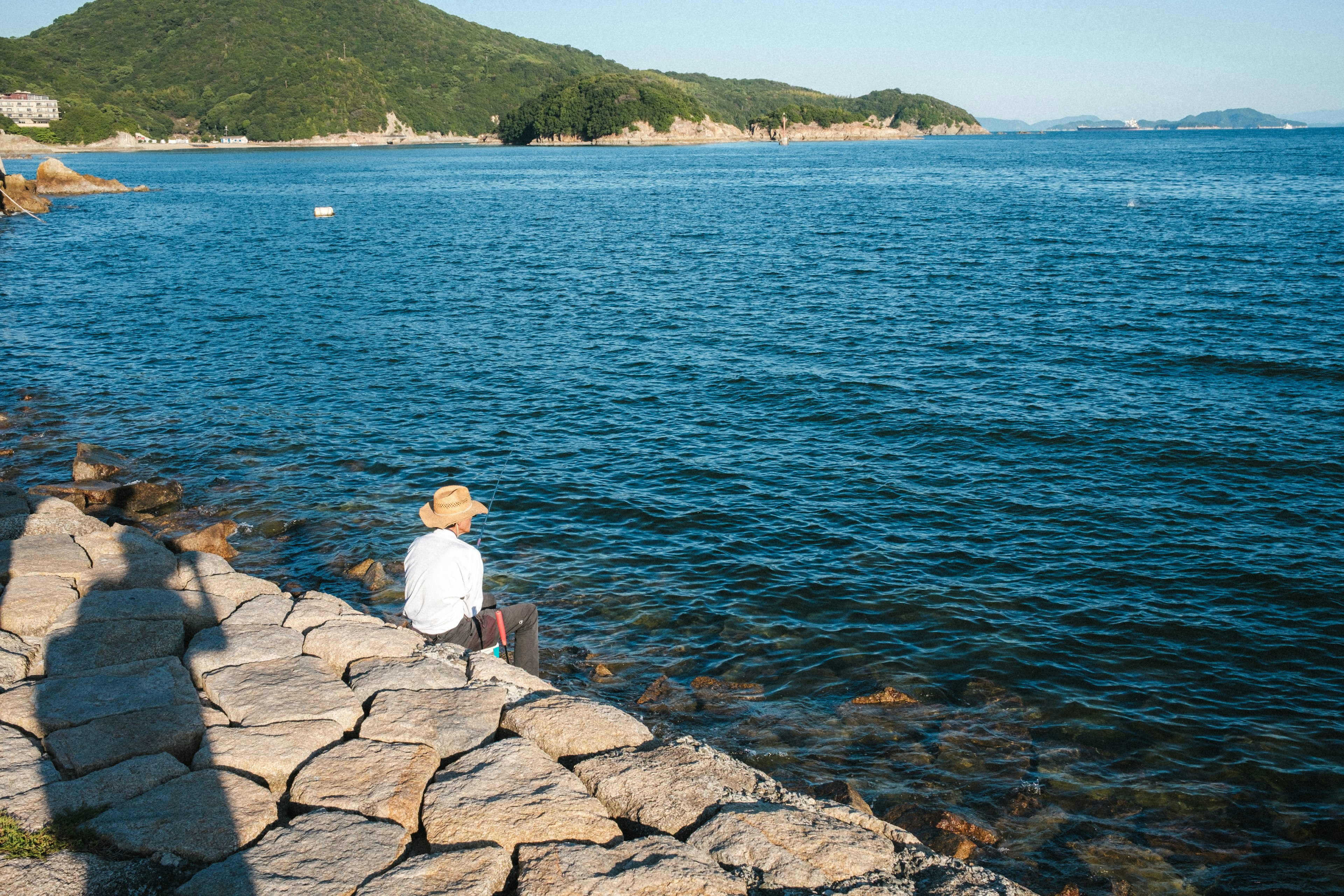 Personne assise au bord de l'eau avec une surface calme et des collines au loin