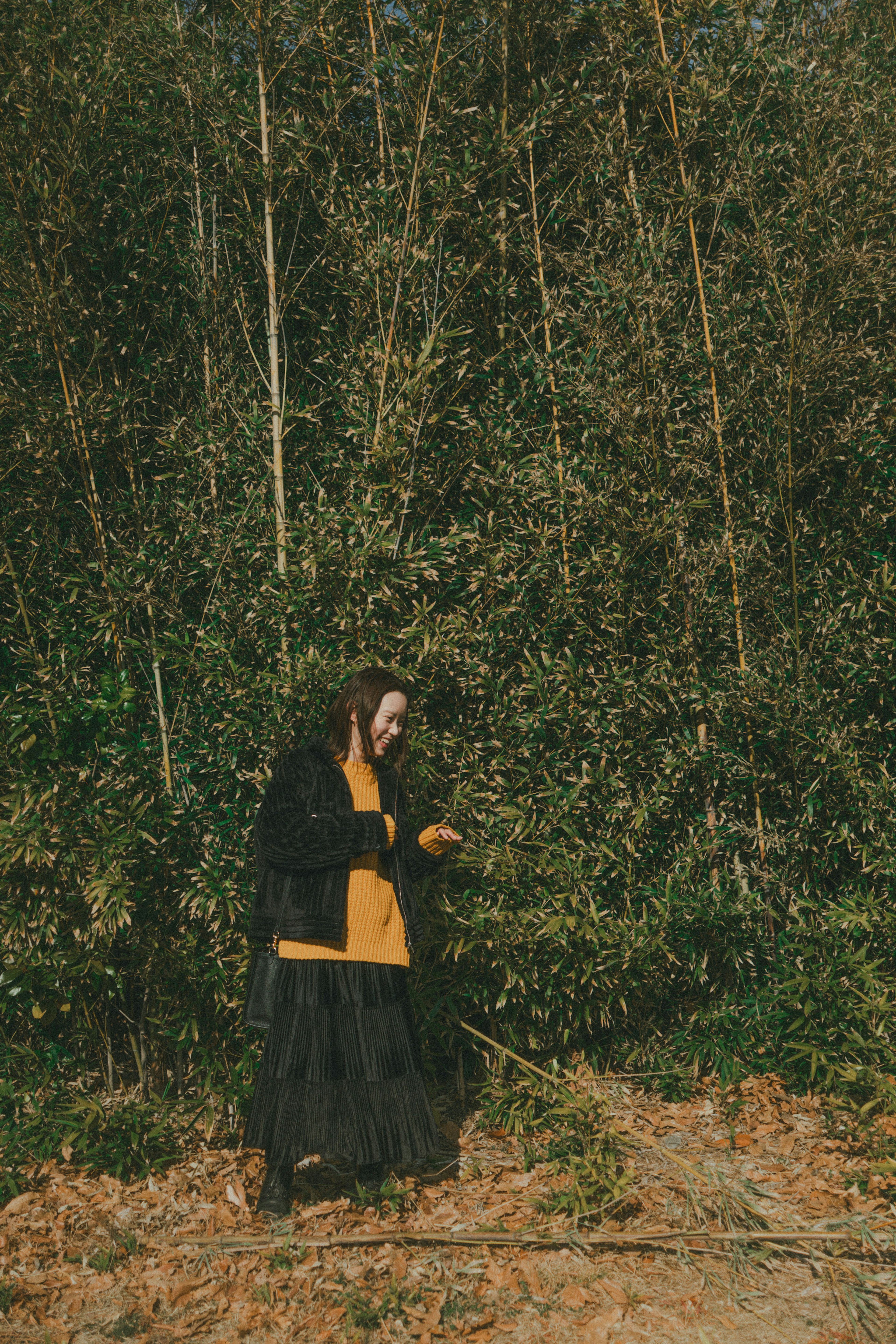 Une femme portant un manteau noir et un haut jaune se tenant dans un cadre forestier