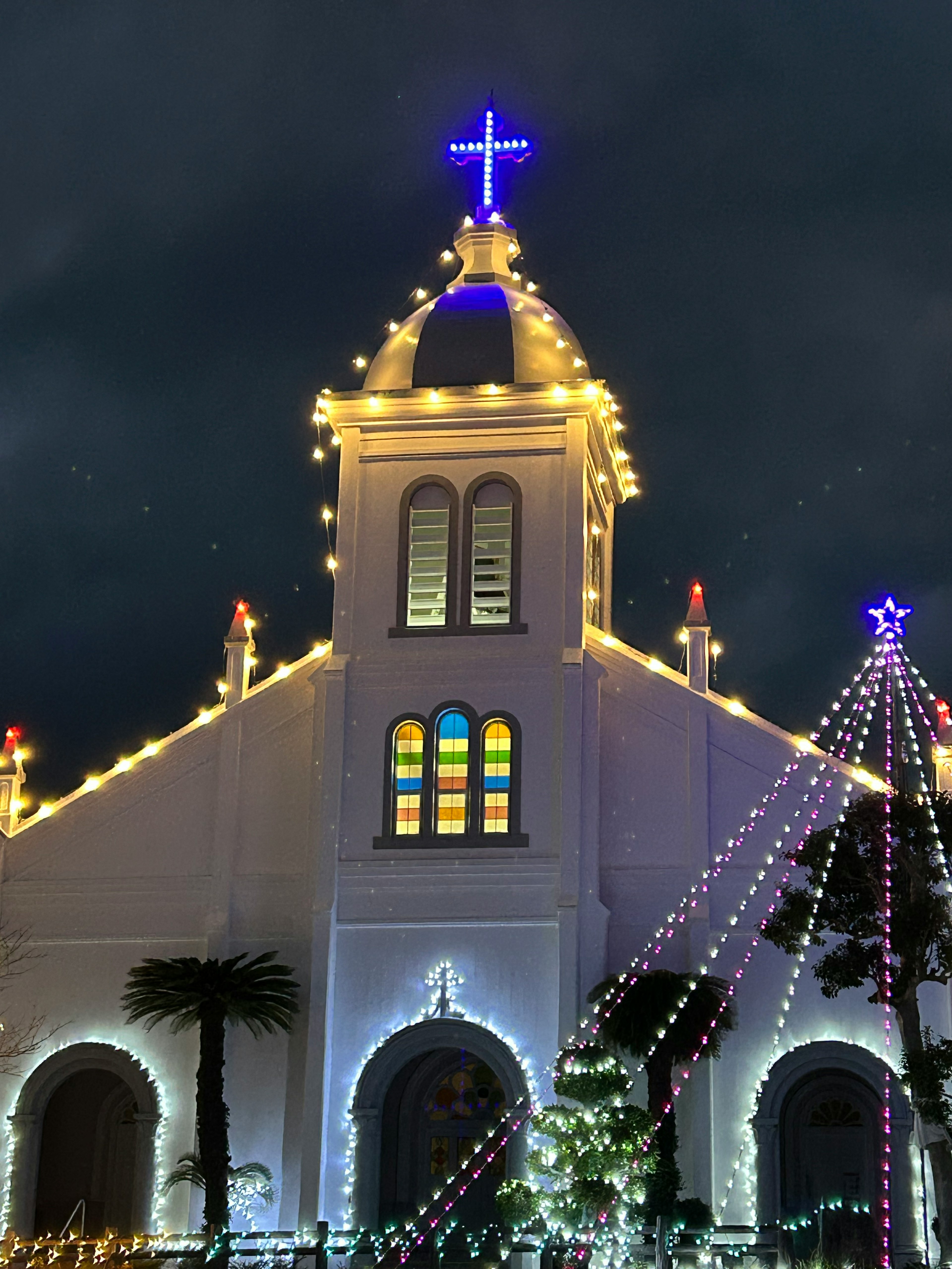 Iglesia iluminada con luces navideñas de noche con una cruz prominente