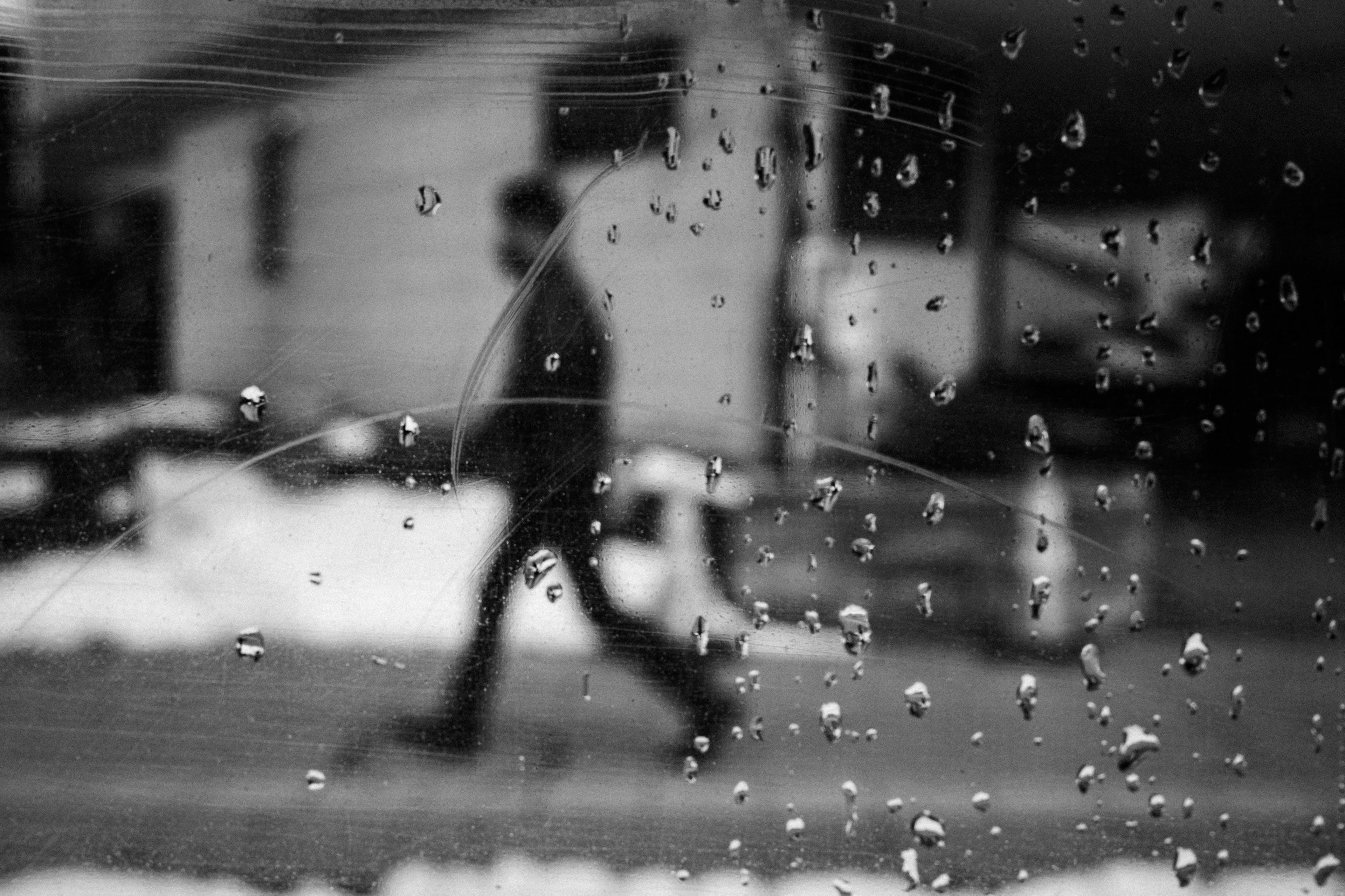 Silhouette of a person walking on snow with raindrops on the window