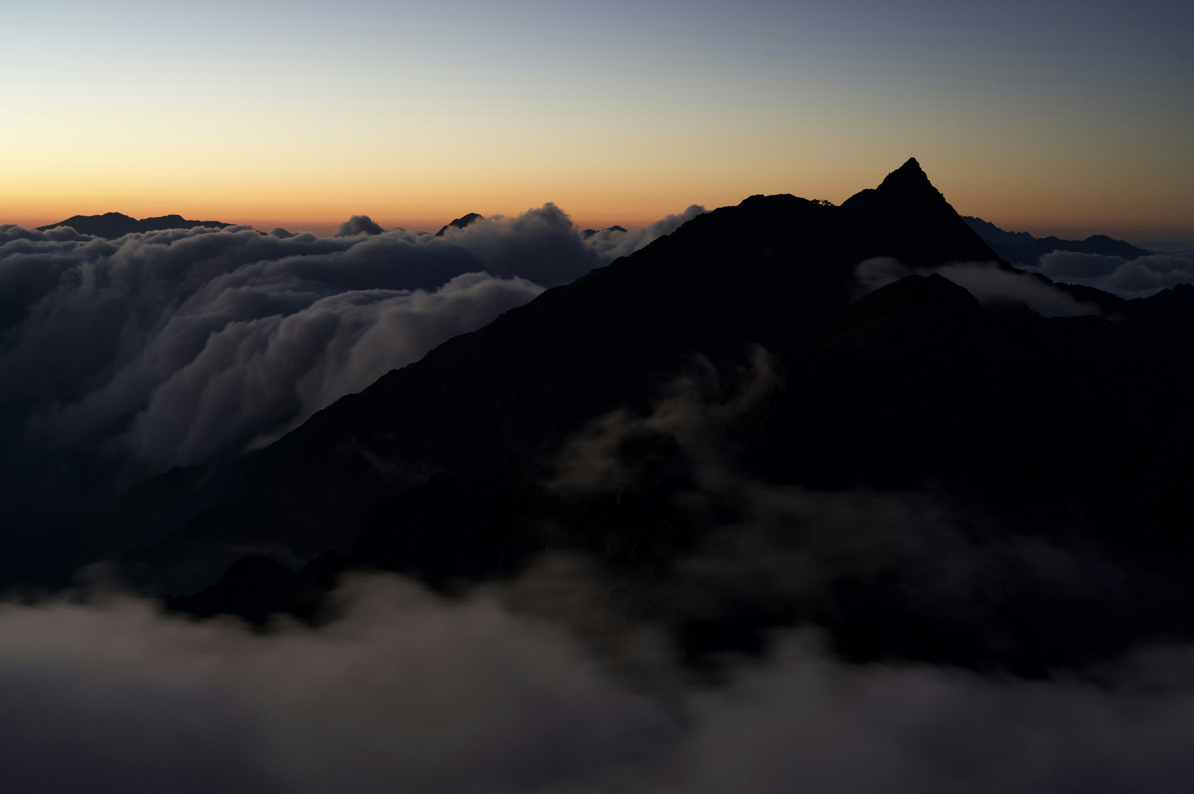 Silhouette of a mountain above a sea of clouds during dawn