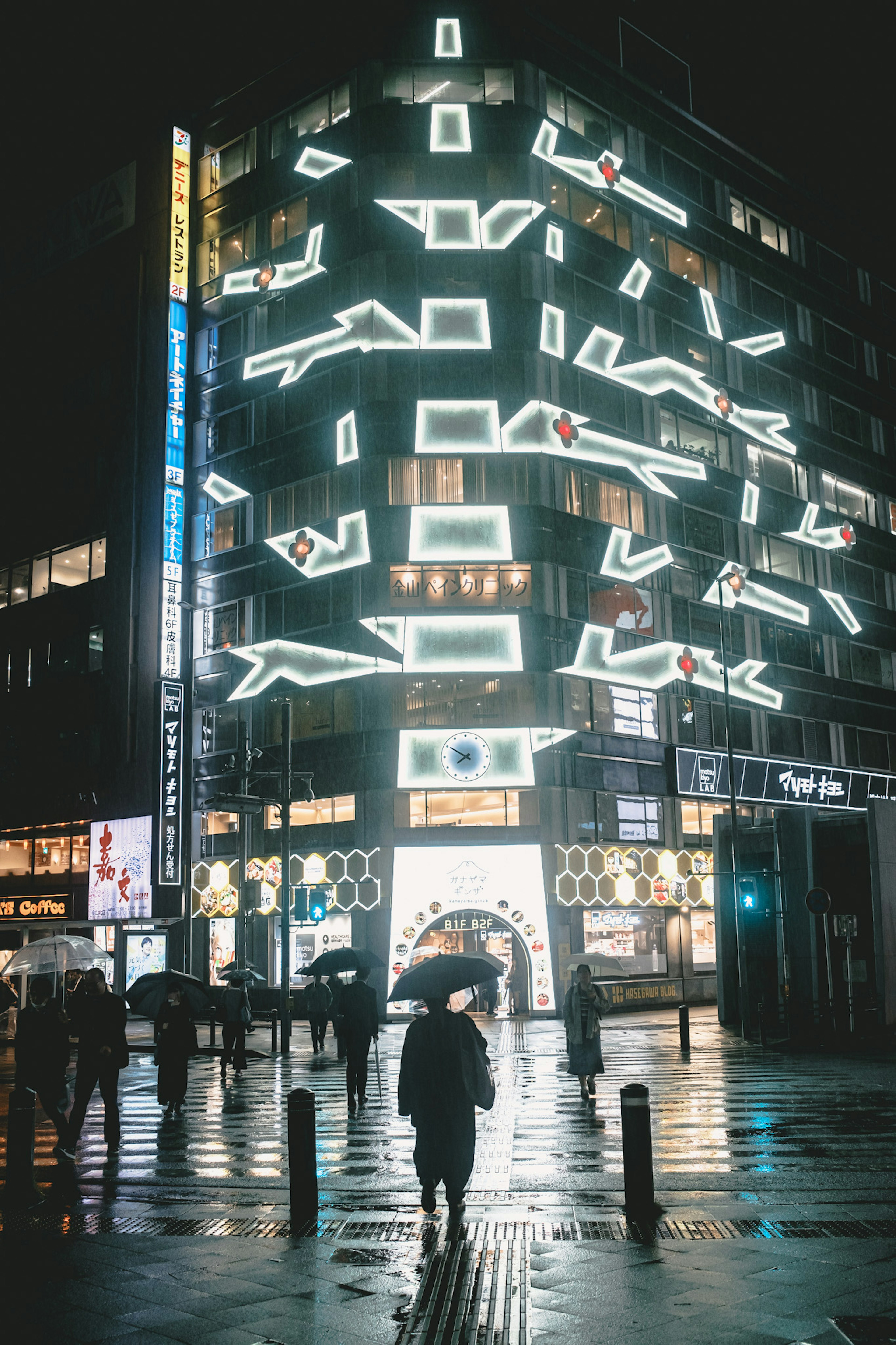 Un edificio iluminado por neón de noche y una persona con un paraguas