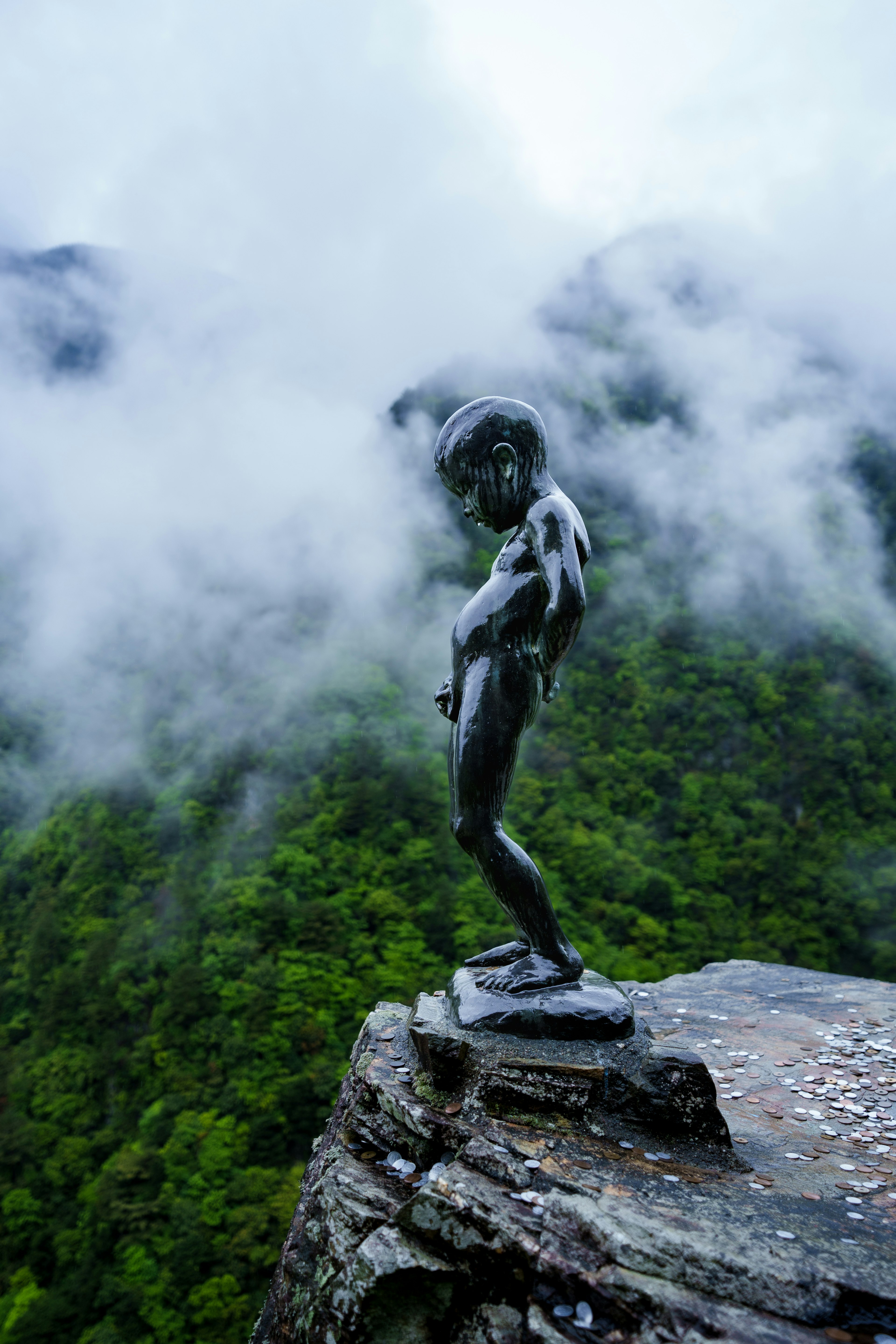 A small bronze statue stands on a cliff surrounded by misty mountains