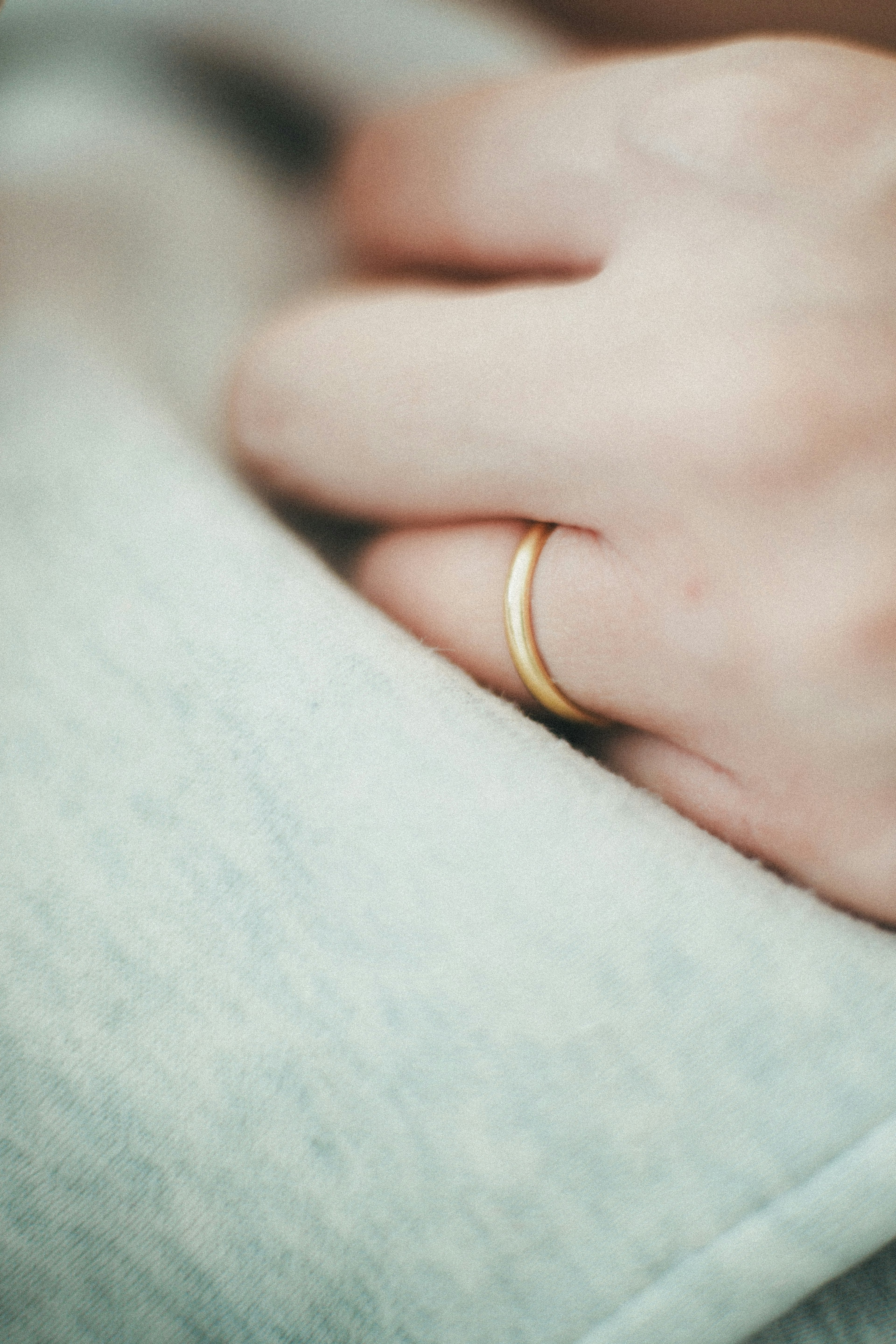 A hand wearing a gold ring resting on soft gray fabric