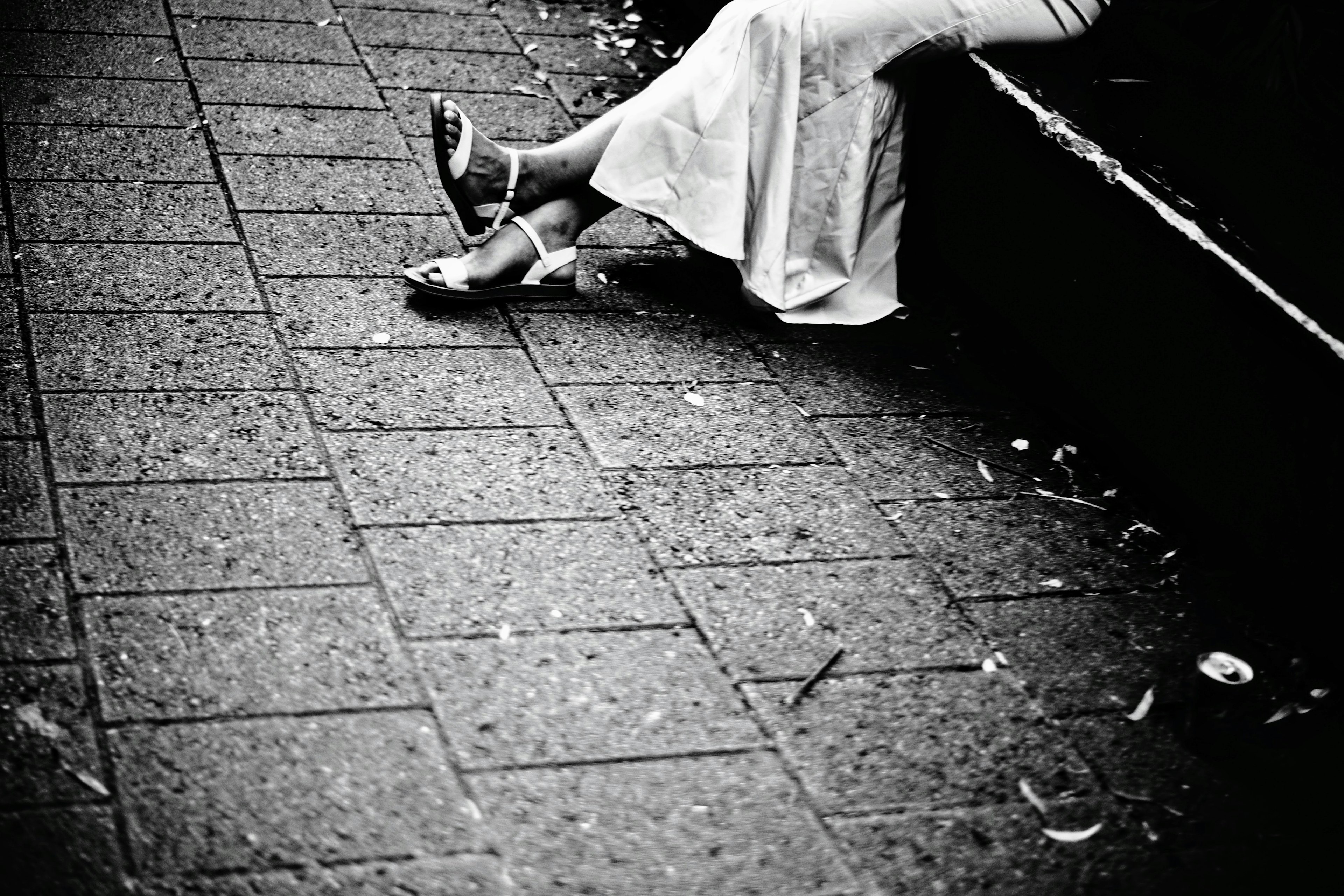 Black and white photo of a woman's feet in a white dress resting on cobblestone pavement