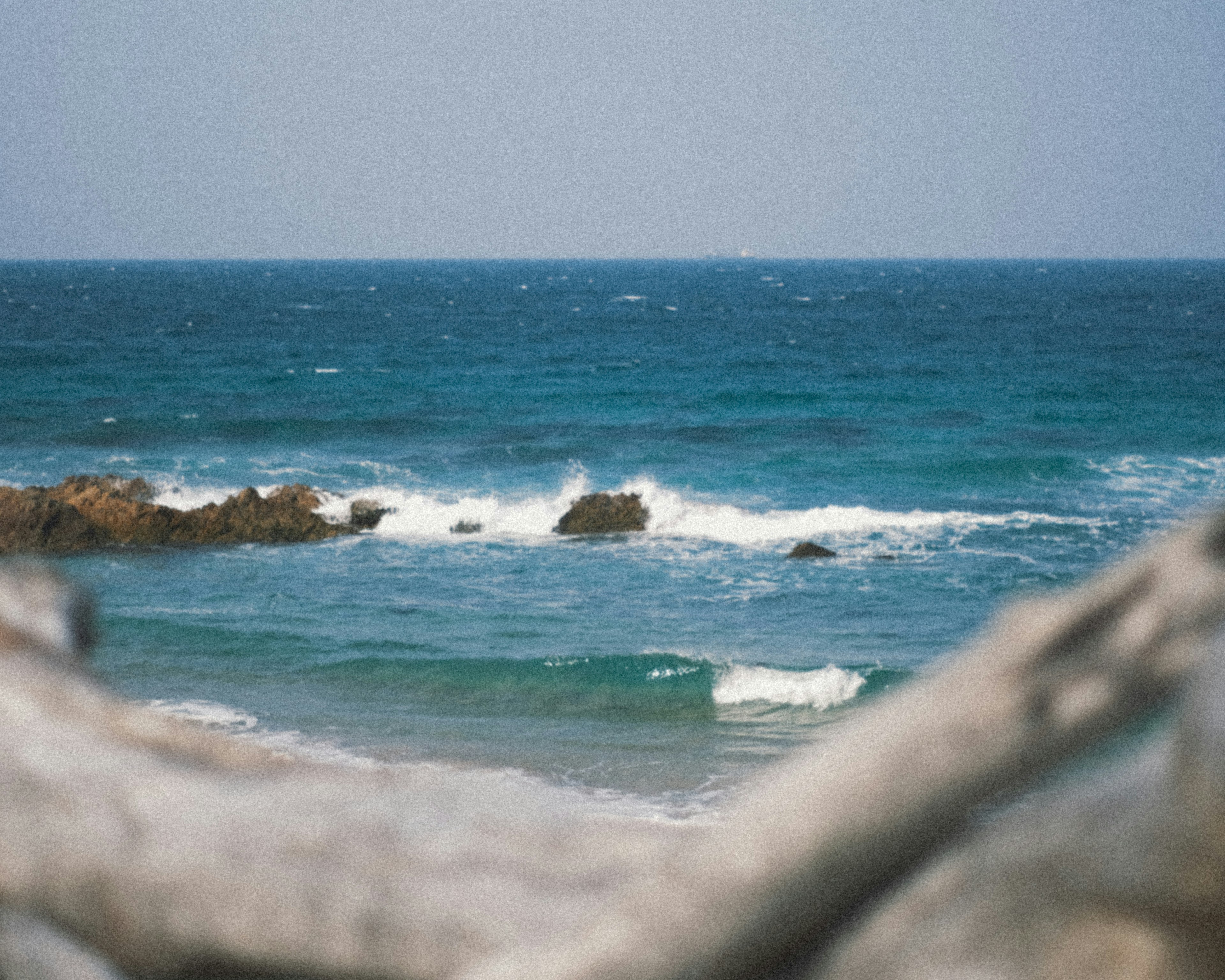 Pemandangan laut biru dengan ombak di pantai dan kayu apung di latar depan