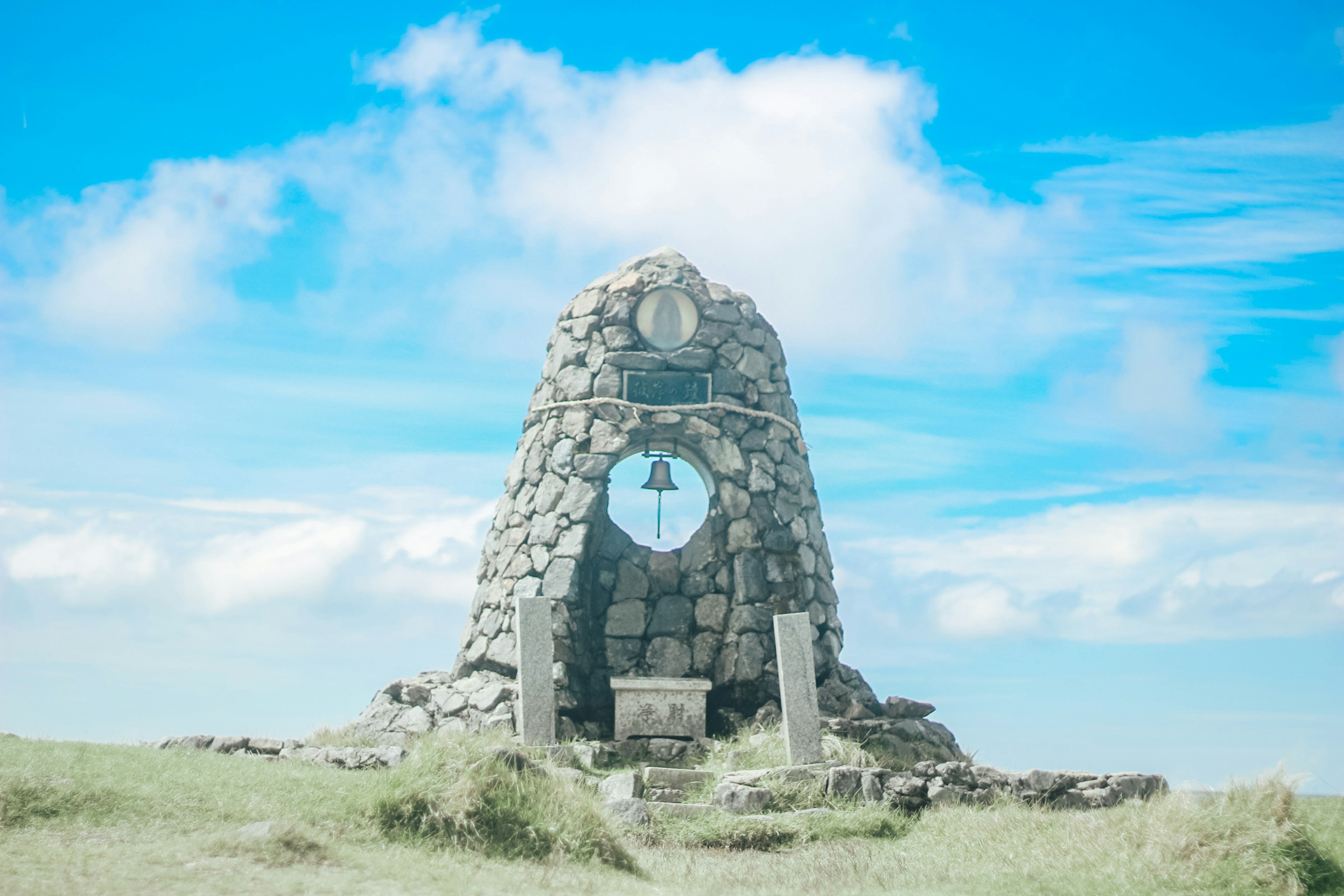 Stone monument with a bell under a blue sky