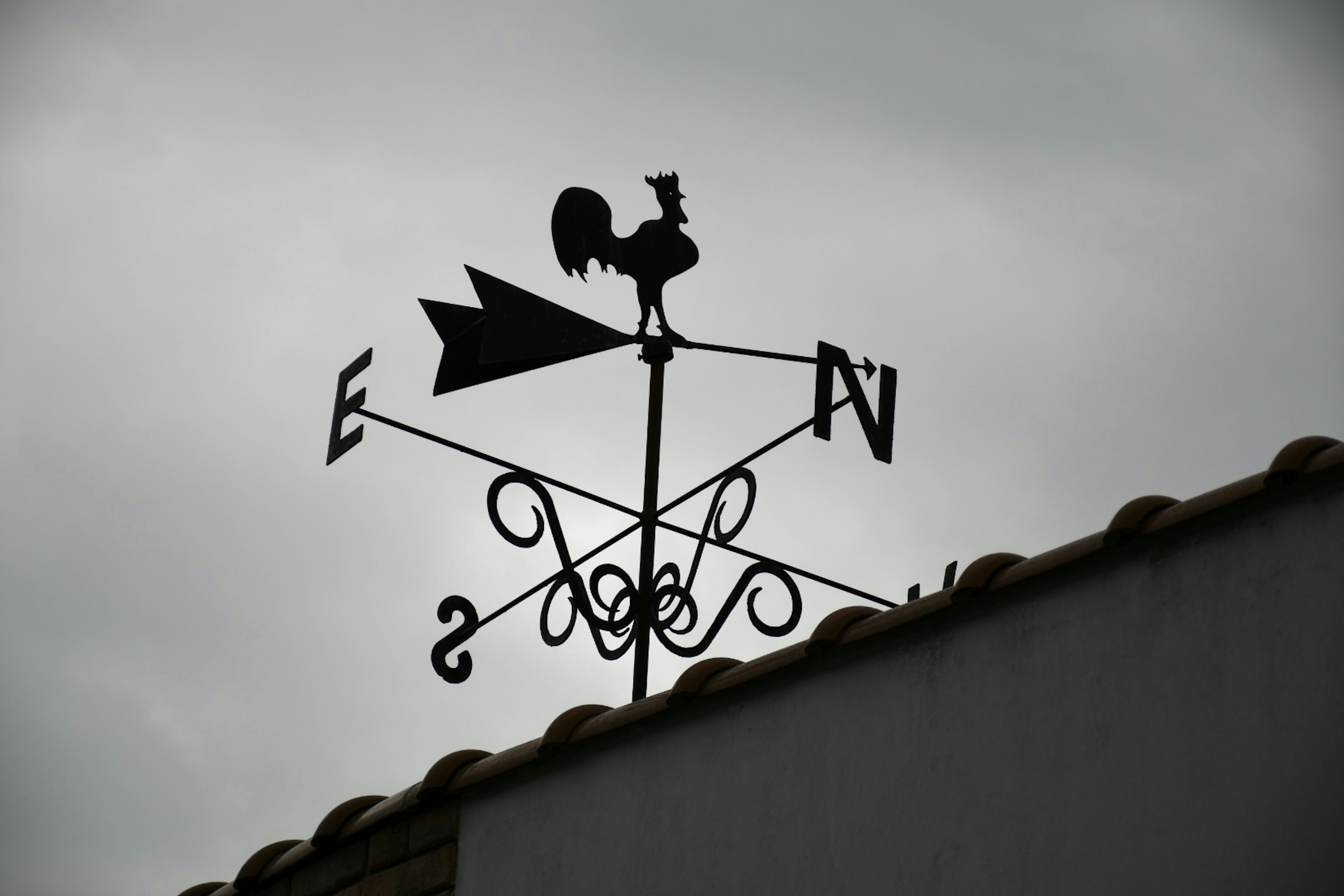 Vane météorologique noire avec silhouette de coq et flèches directionnelles sur un toit