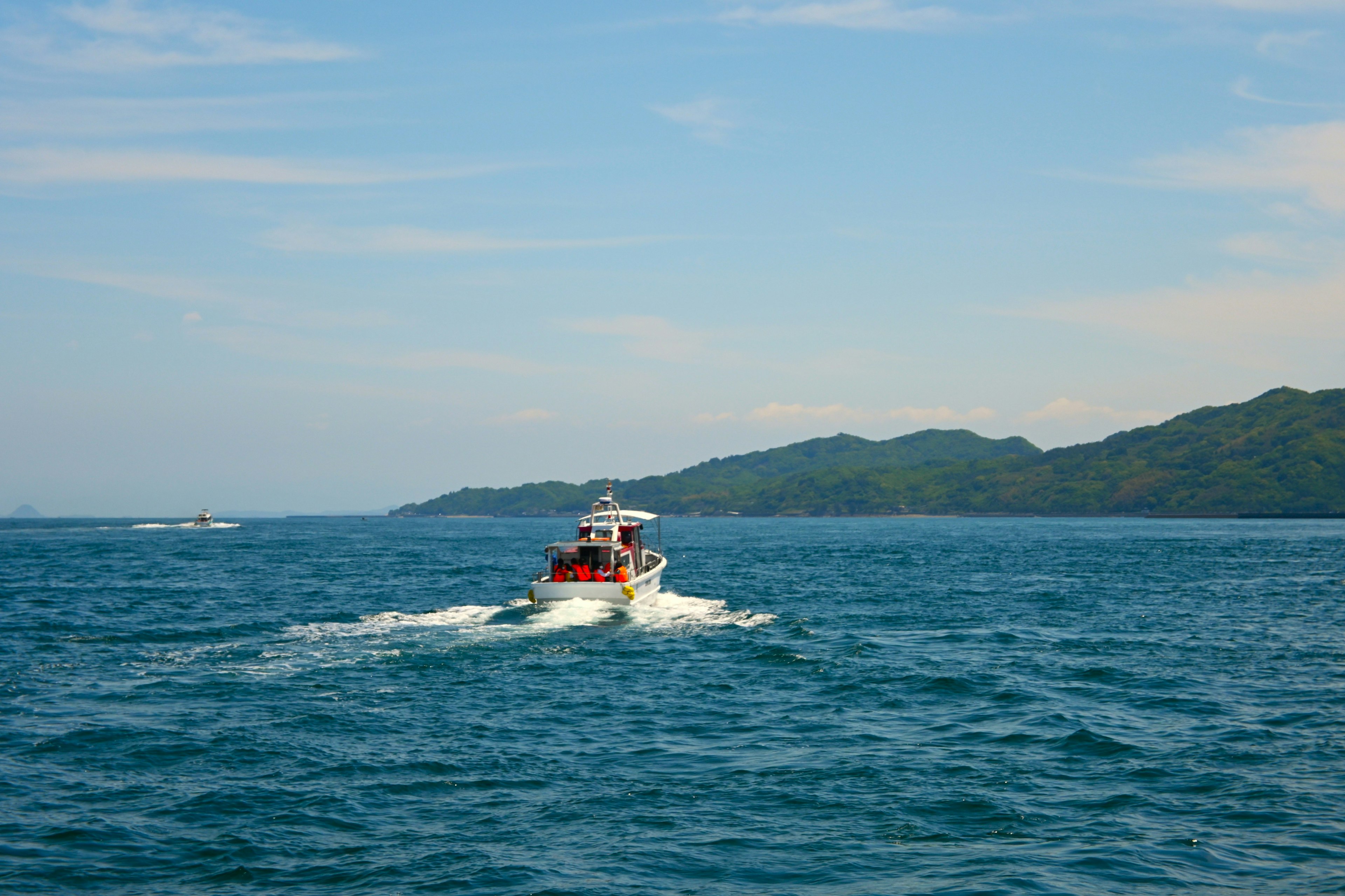 Red boat navigating on blue sea with green hills in the background