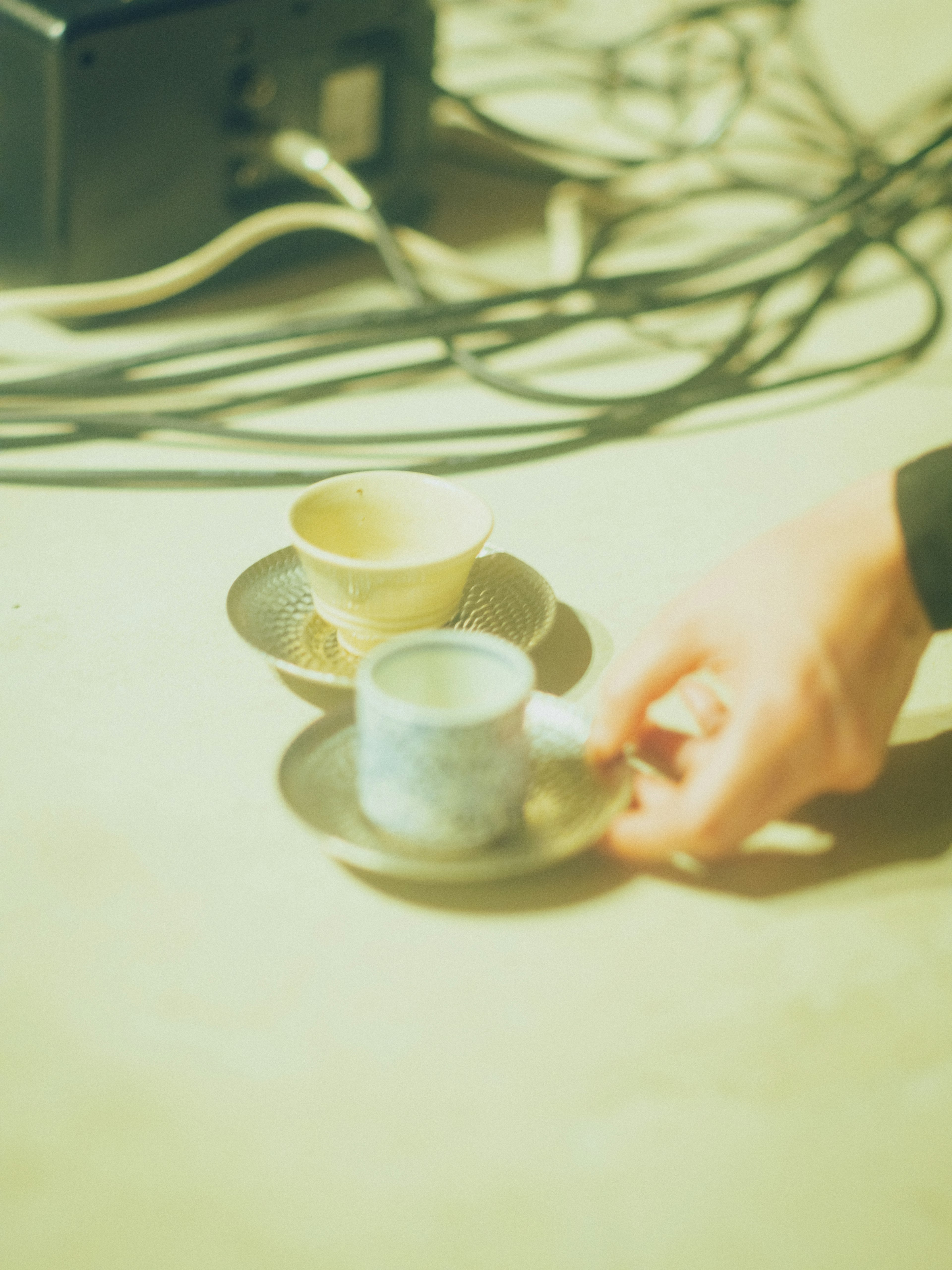 A hand holding a blue cup and a yellow cup on a plate with cables scattered around