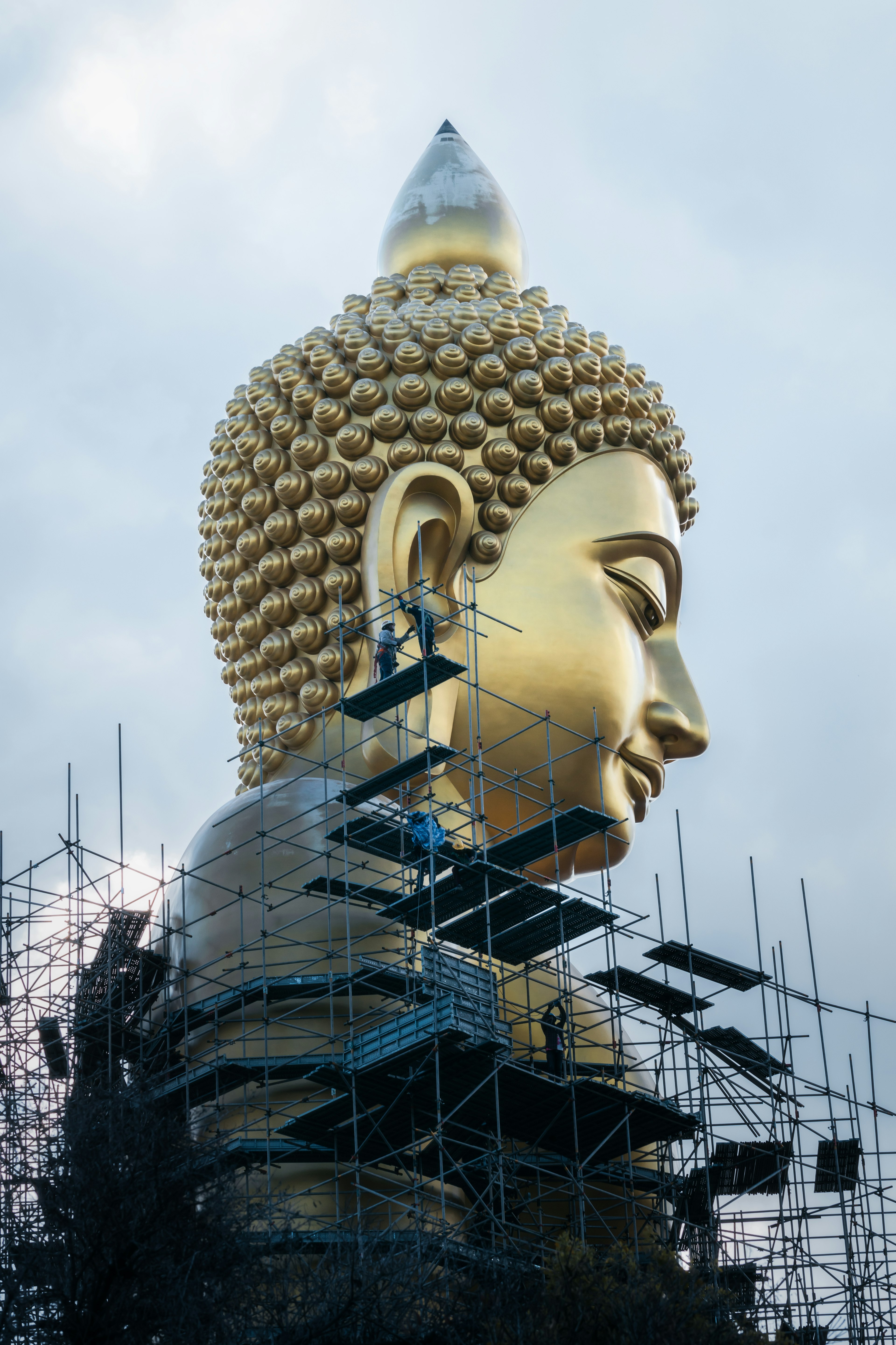 Tampak samping patung Buddha besar berwarna emas dengan perancah