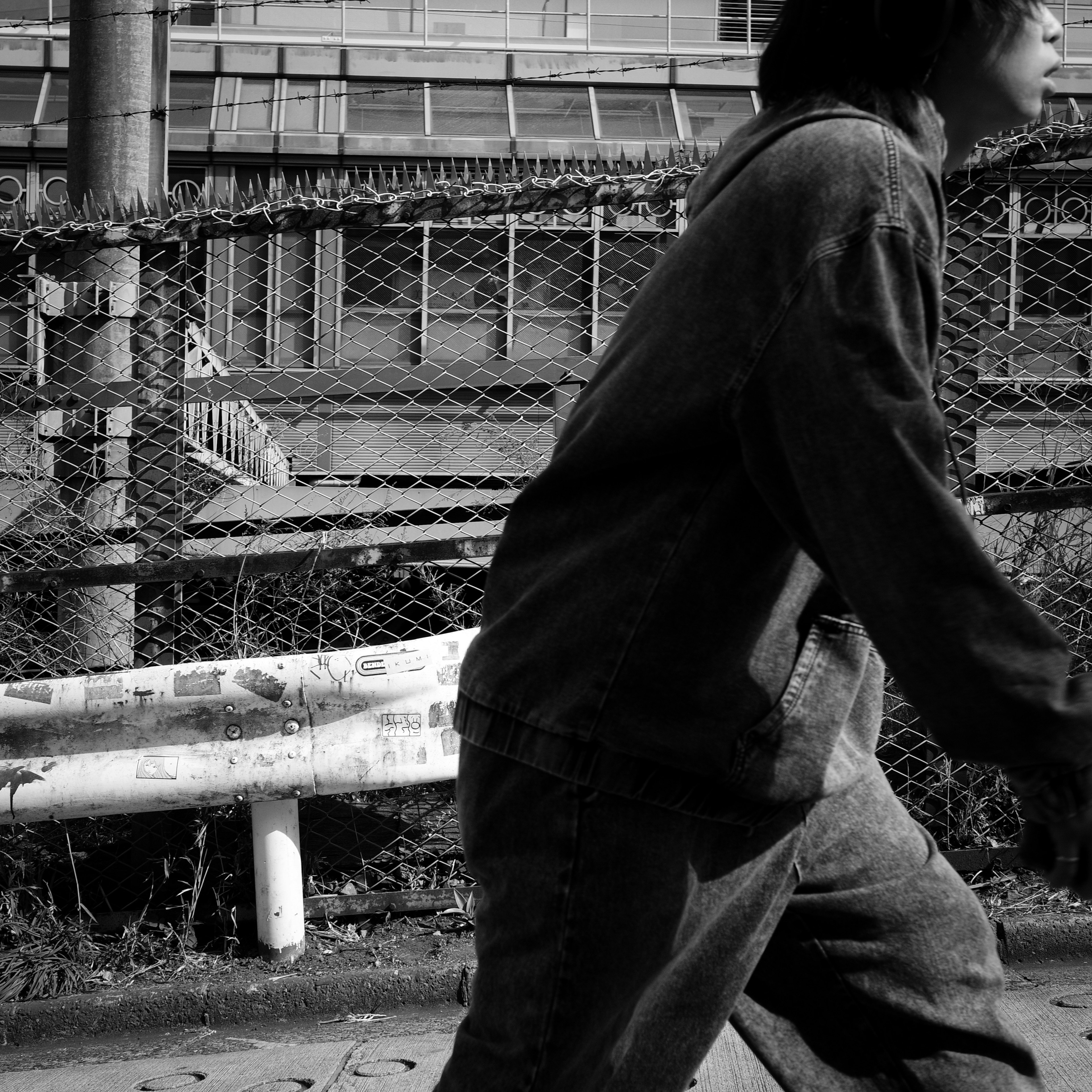 A person walking in a black and white urban setting with a fence in the background