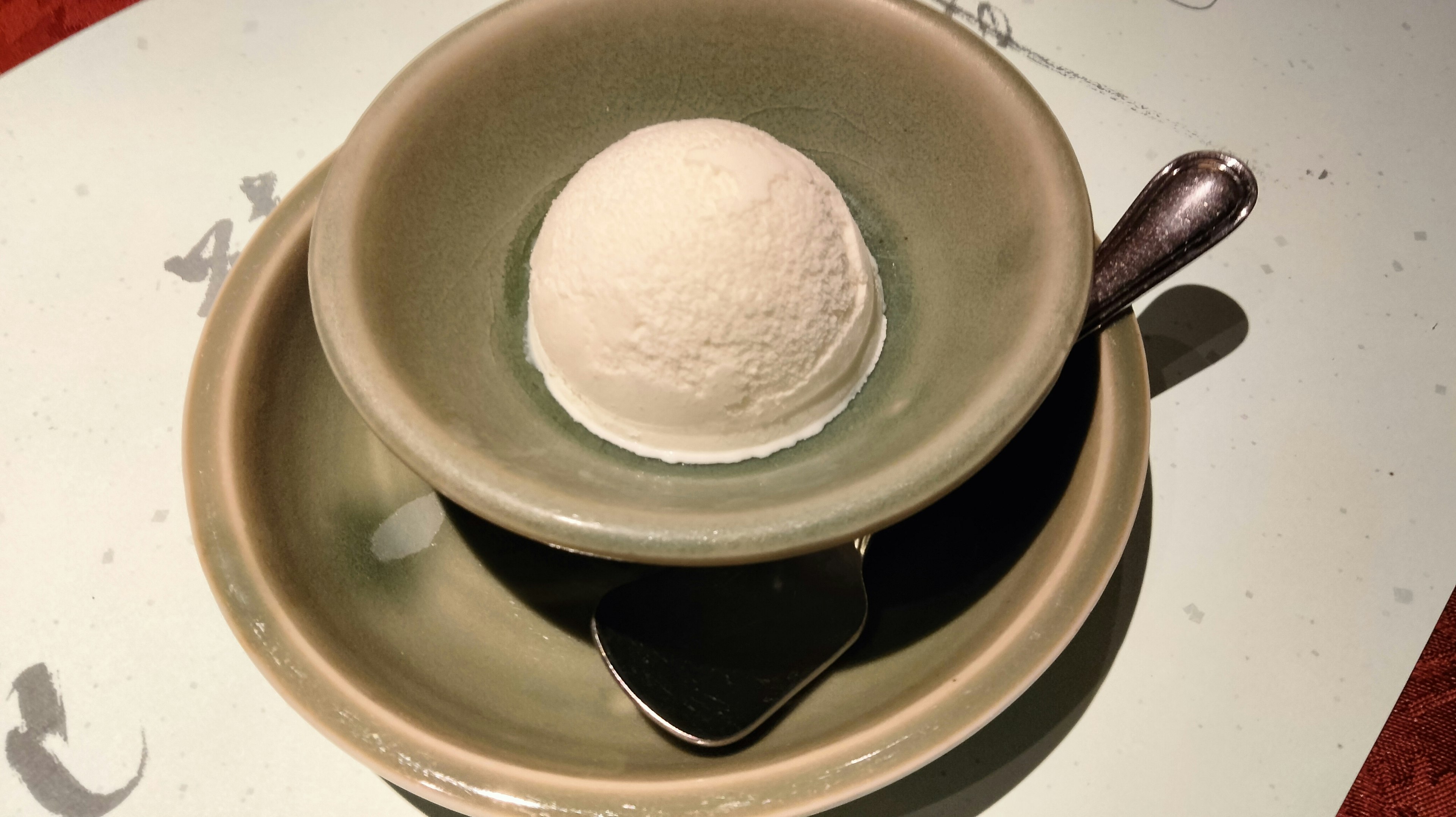 Round ice cream served in a green bowl on top of a larger plate