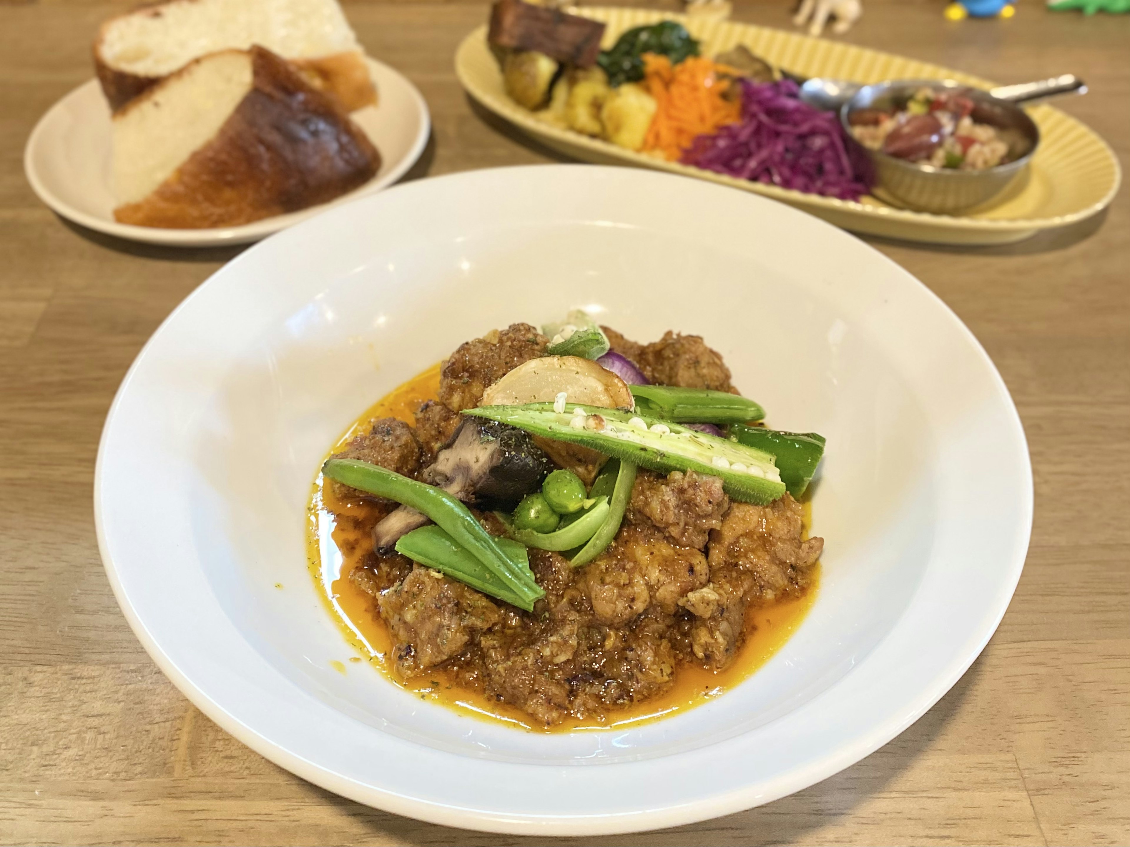 Ein Fleischgericht mit Frühlingszwiebeln in einer weißen Schüssel serviert mit Brot und verschiedenen Beilagen im Hintergrund