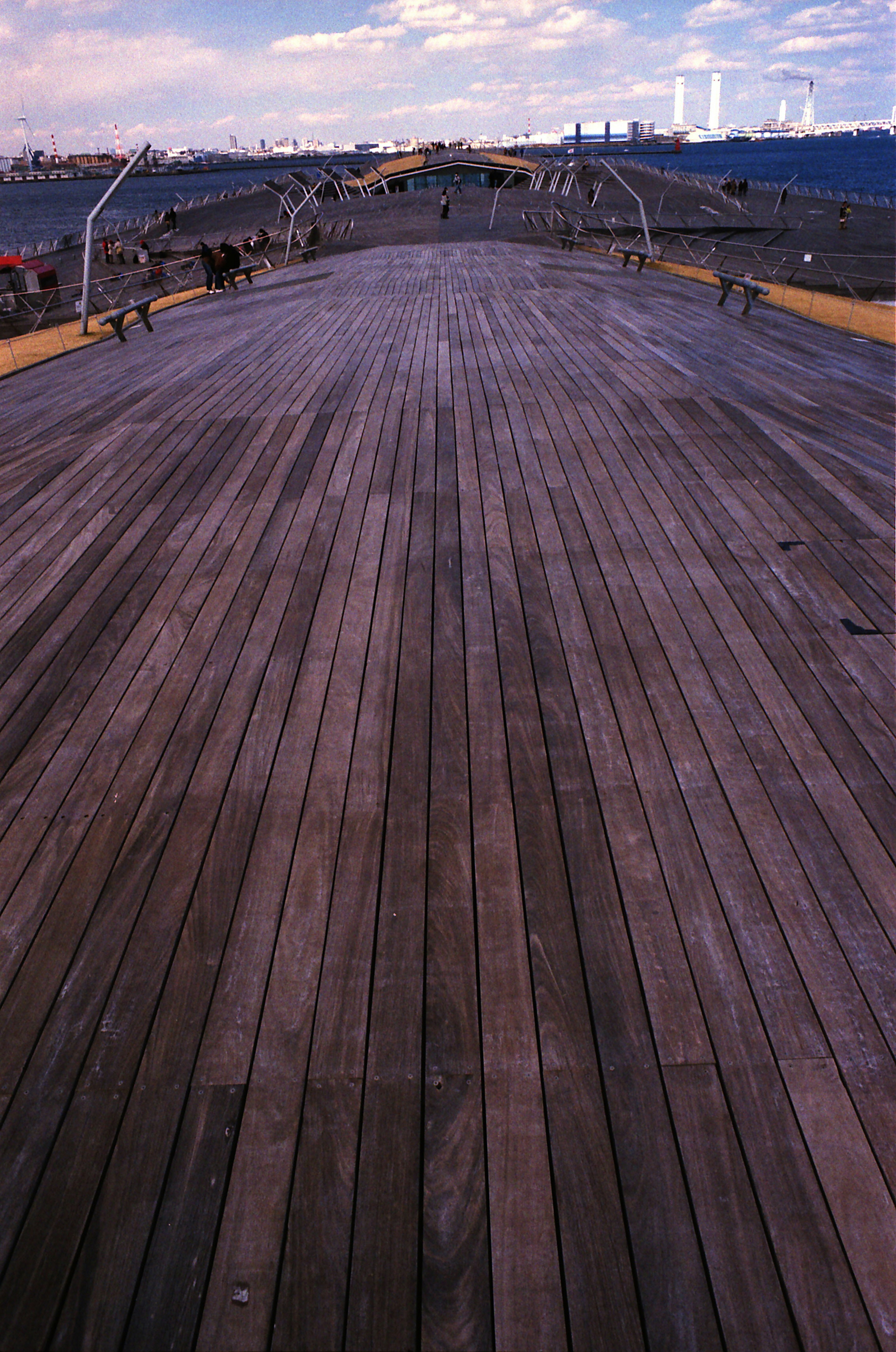 Deck de madera que se extiende en la distancia con un cielo nublado y edificios lejanos