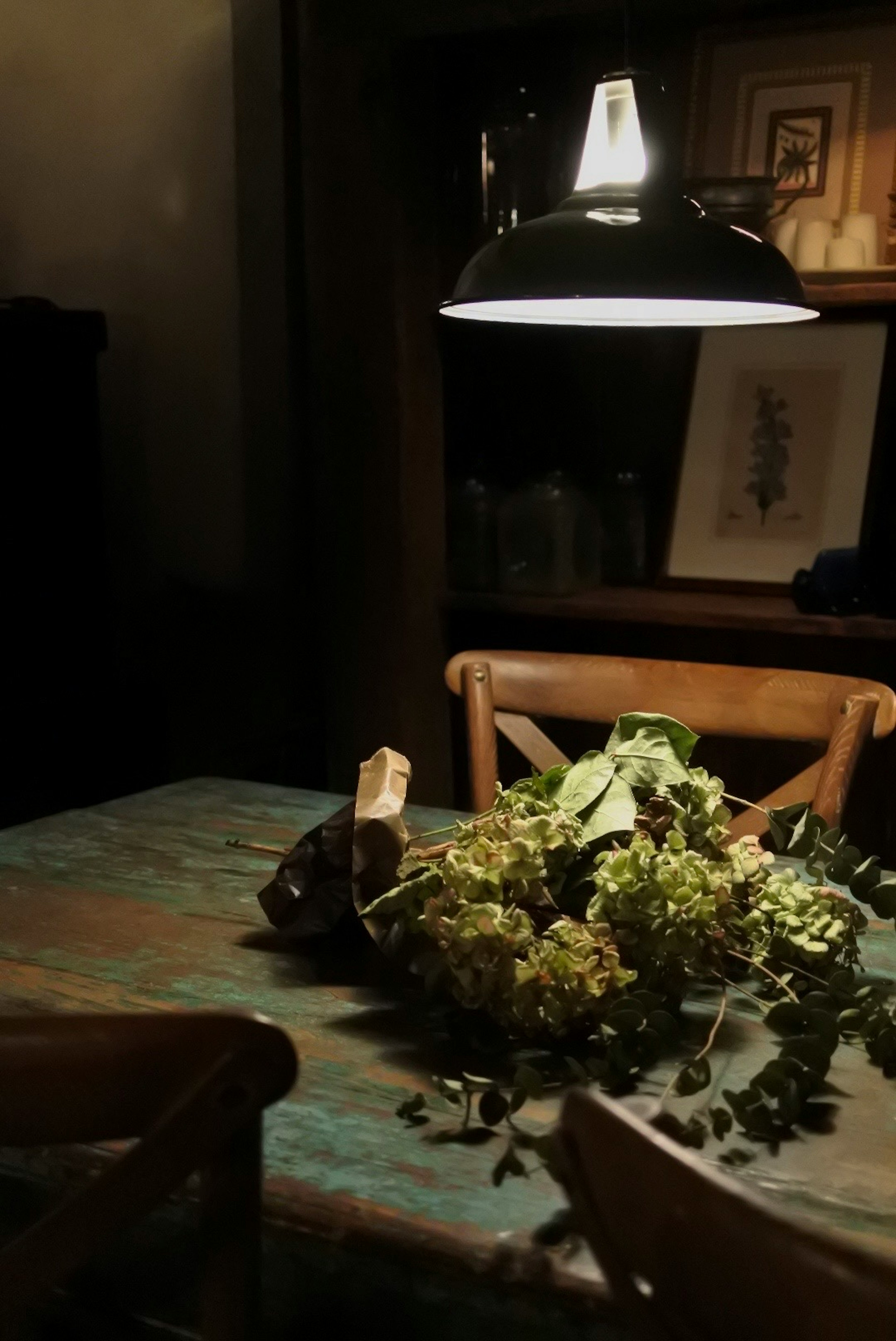 Table en bois avec un arrangement floral dans une pièce faiblement éclairée avec une lampe suspendue