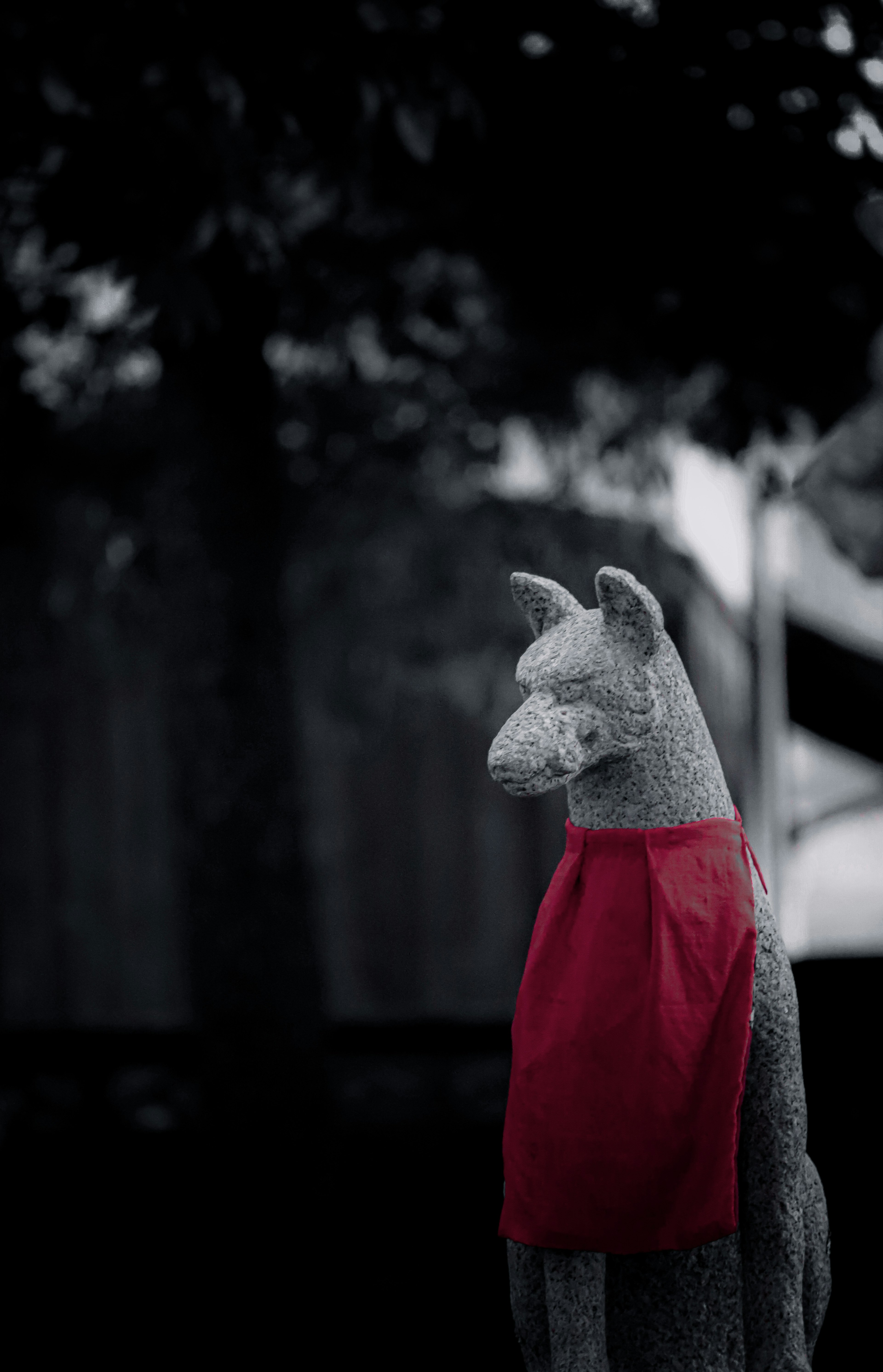 Gray llama statue wearing a red scarf against a black and white background