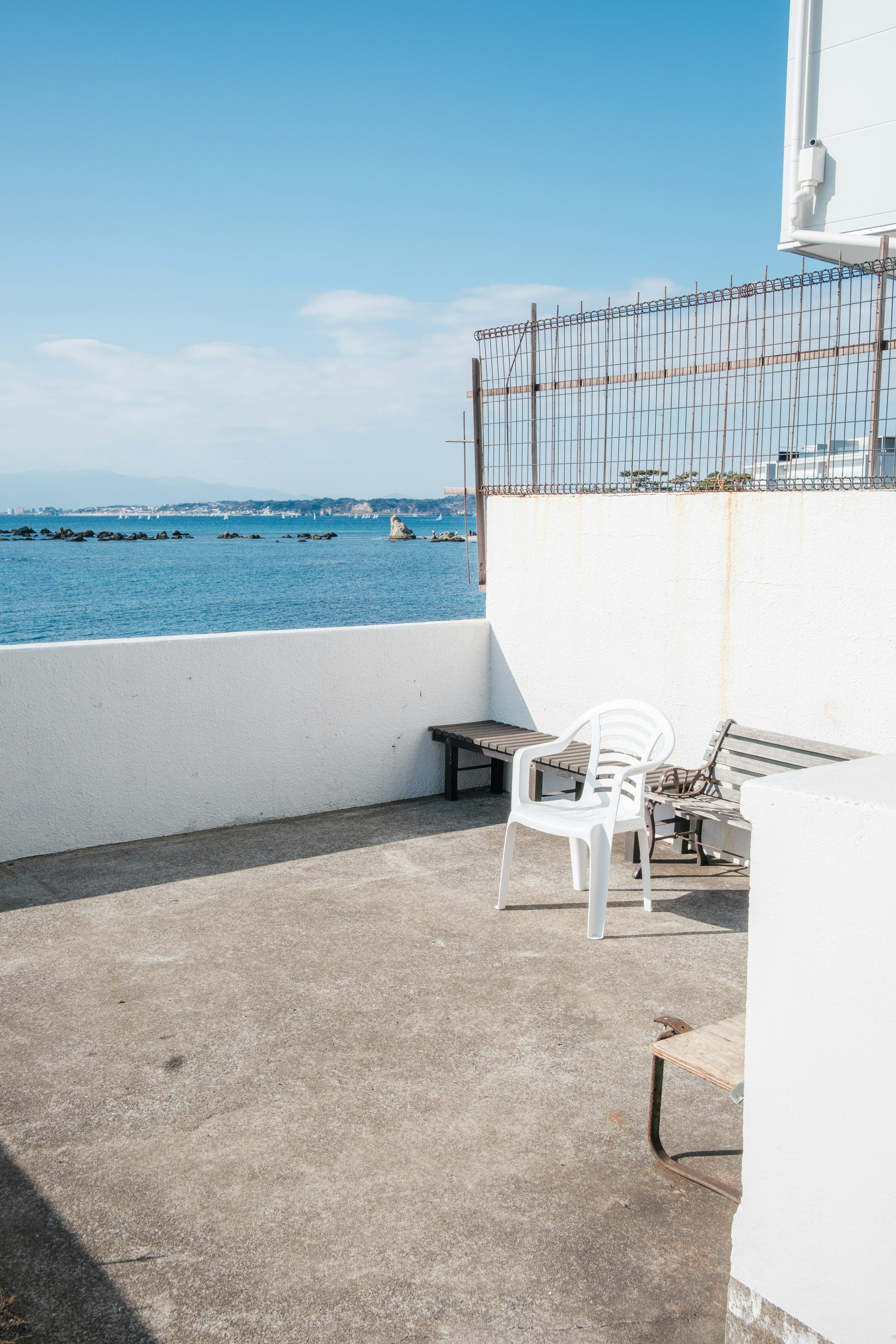 Eine Terrasse mit Blick auf das blaue Meer und den Himmel, weißen Wänden und Stühlen