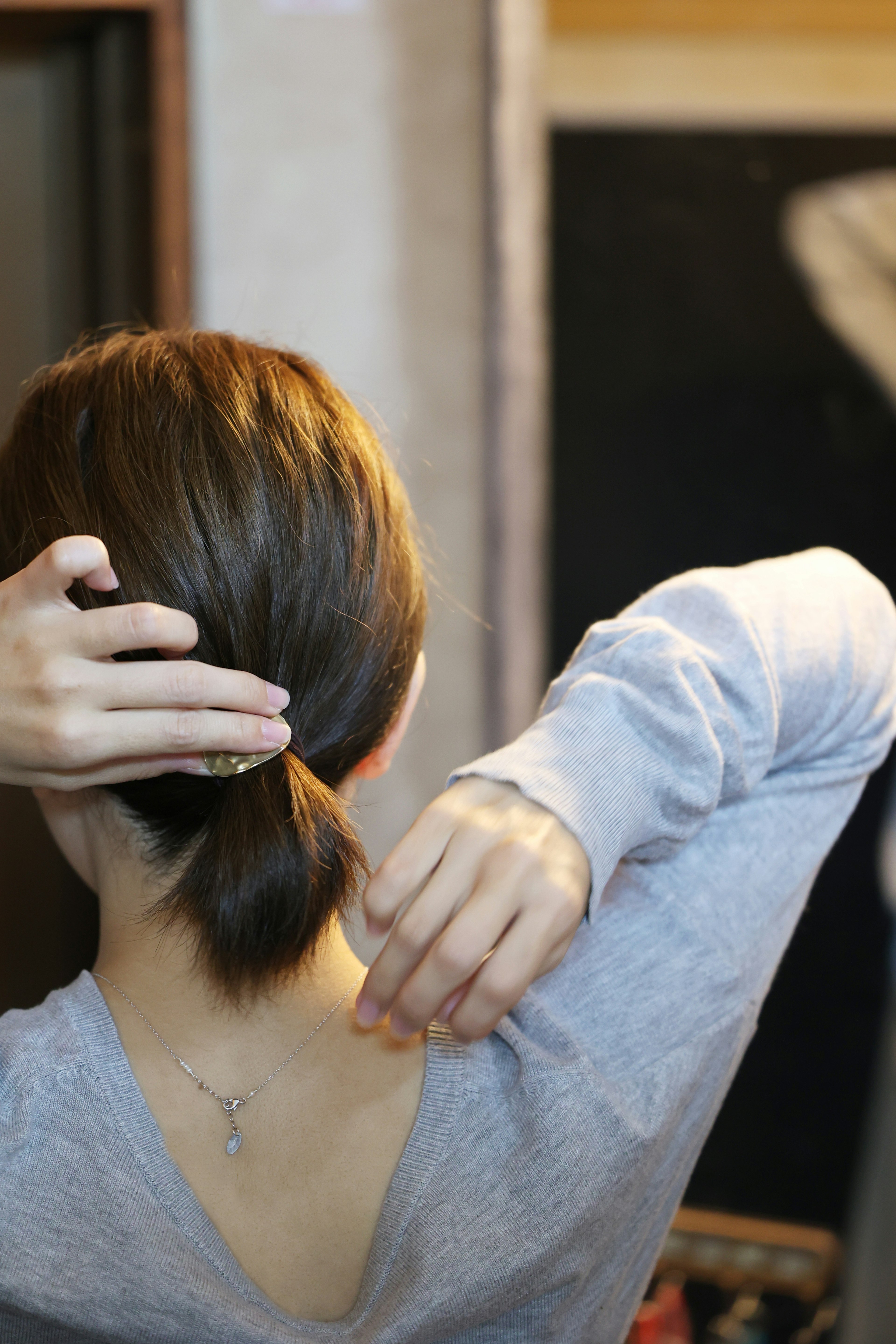 Frau, die sich die Haare von hinten bindet sanfte Farben und warmes Licht