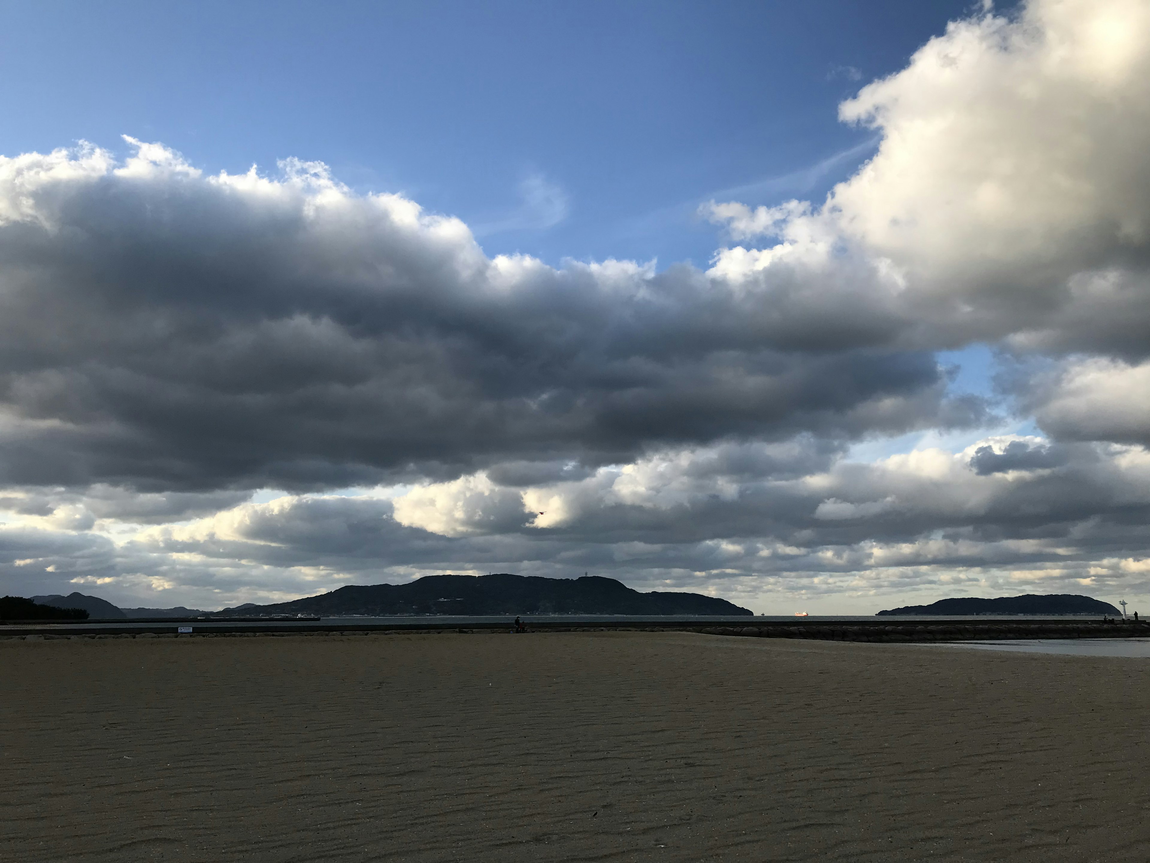 Pantai pasir luas dengan pulau-pulau jauh di bawah langit mendung