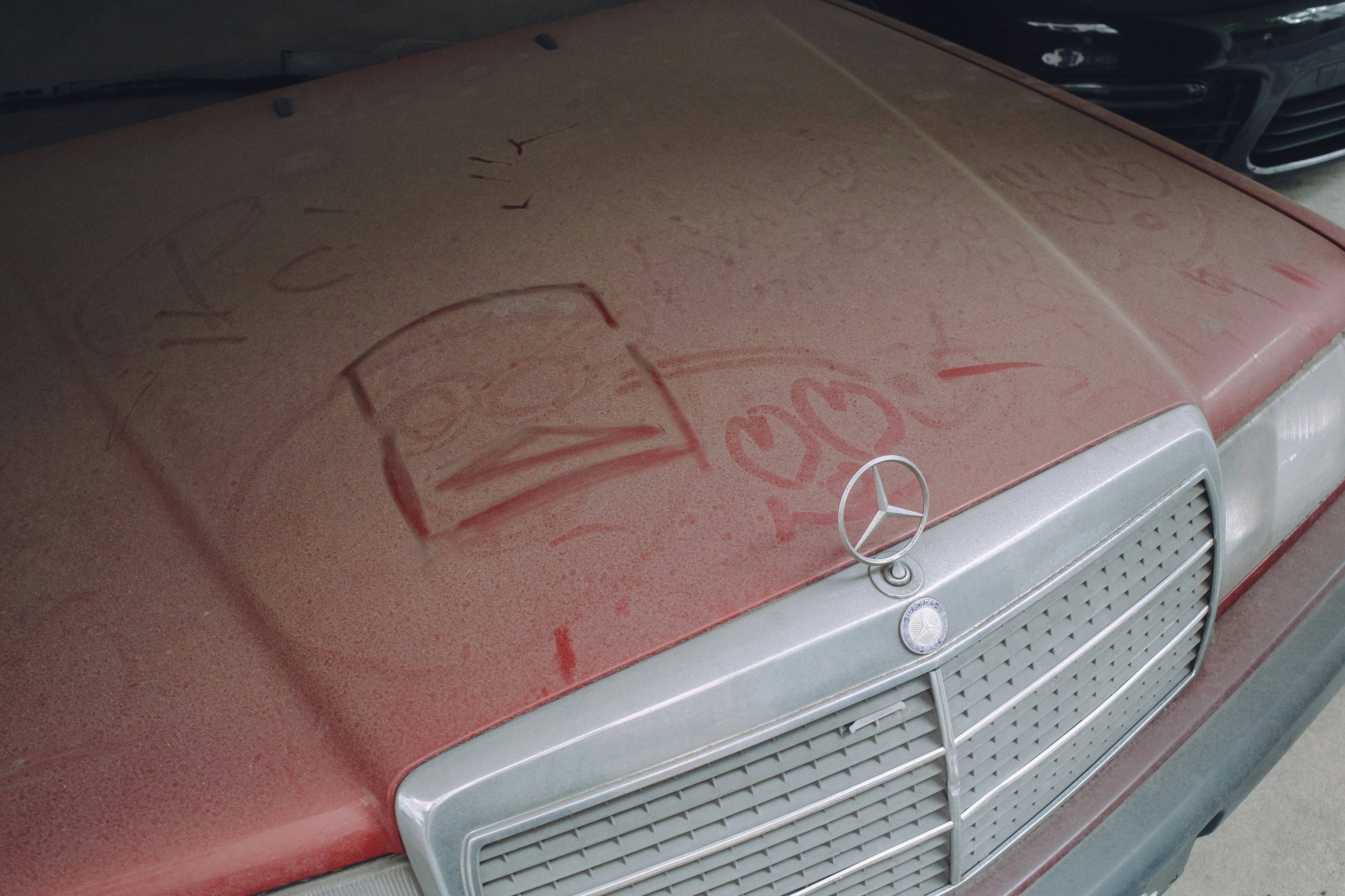 Dust-covered Mercedes hood with graffiti designs