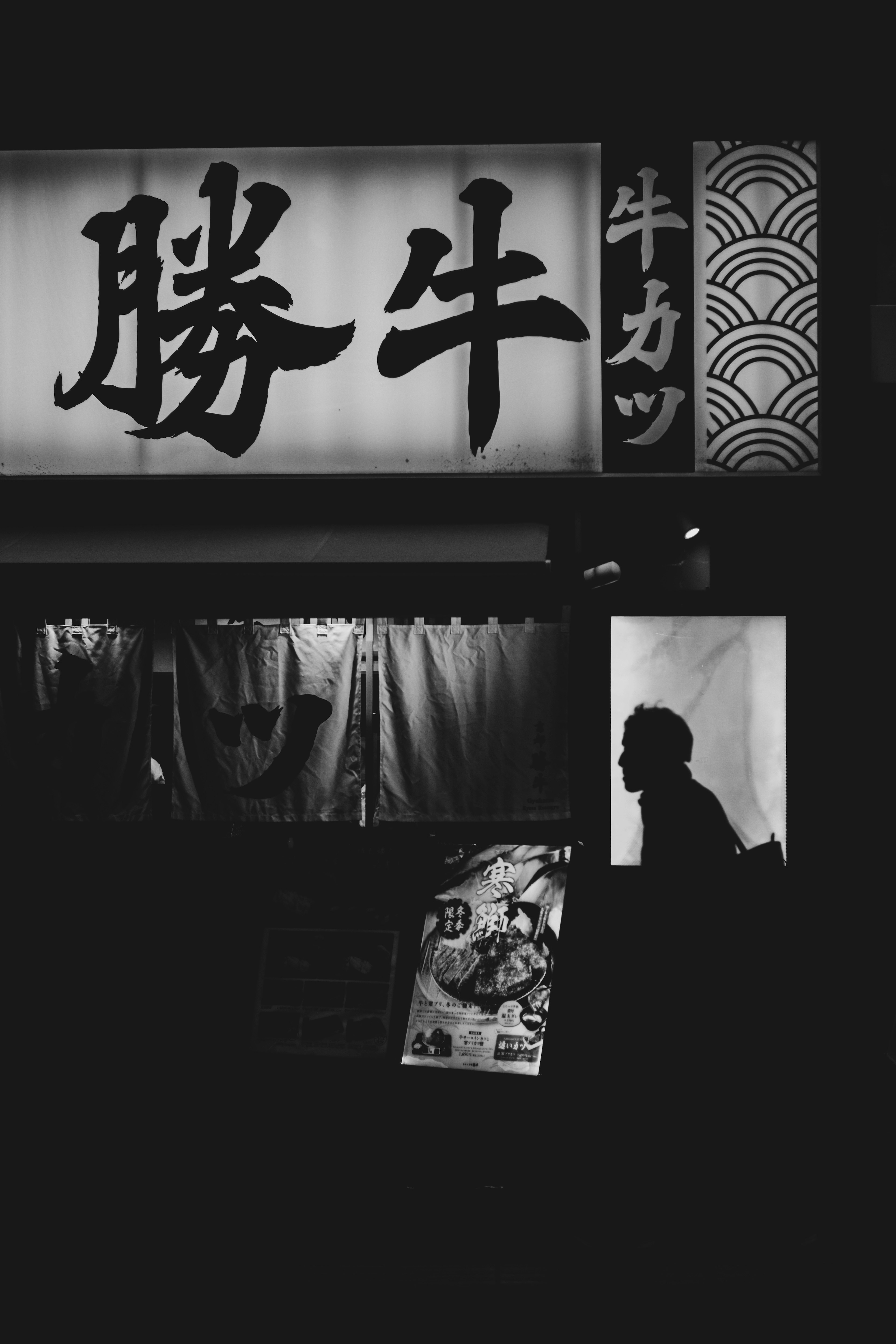 A silhouetted figure in front of a restaurant sign in black and white